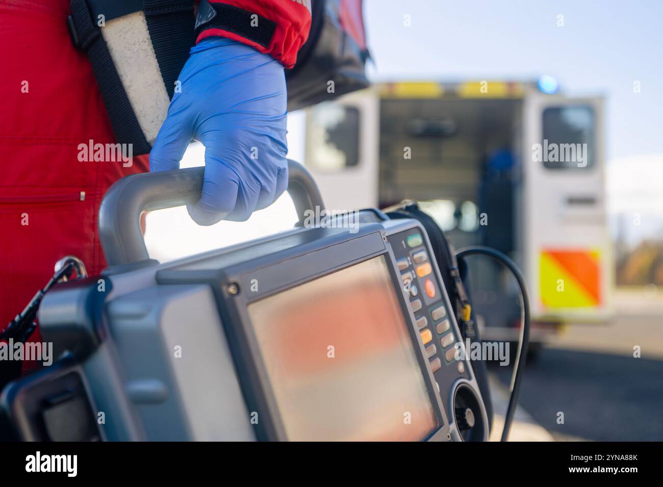 Ärztlicher Notdienst. Nahaufnahme der Sanitäter-Hand in blauen Operationshandschuhen beim Laufen mit Defibrillator-Monitor gegen Ambulanzwagen. Themes r Stockfoto
