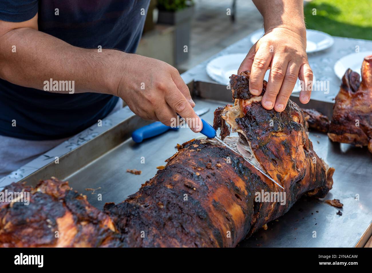 Die Hände des Mannes schneiden ganze Ferkel, gebacken auf einem Spieß. Stockfoto