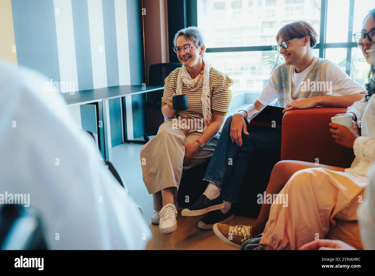 Ein reifer Lehrer teilt eine Kaffeepause mit den Schülern während einer entspannten Unterrichtsdiskussion, um eine komfortable Lernumgebung in einem modernen e zu schaffen Stockfoto