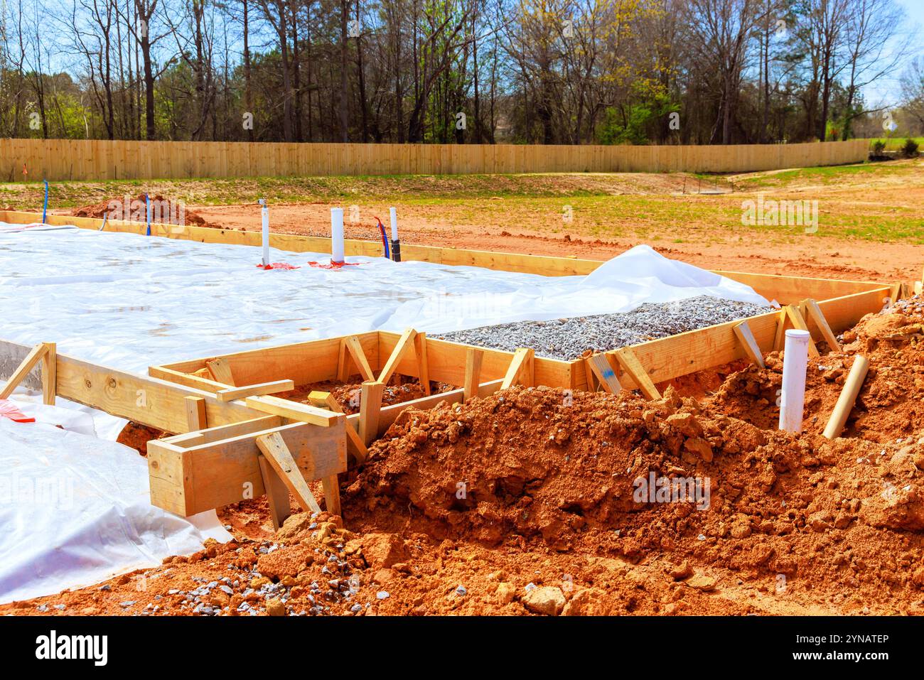 Vorbereitung des Fundaments auf der Baustelle mit Holzformen, die mit Kies gefüllt sind und von einem mit Kunststoff bedeckten Bereich umgeben sind, um Feuchtigkeit zu verhindern Stockfoto