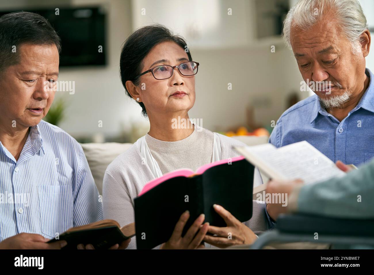 Eine Gruppe asiatischer Senioren sitzt zu Hause auf der Couch und liest gemeinsam Bibel Stockfoto