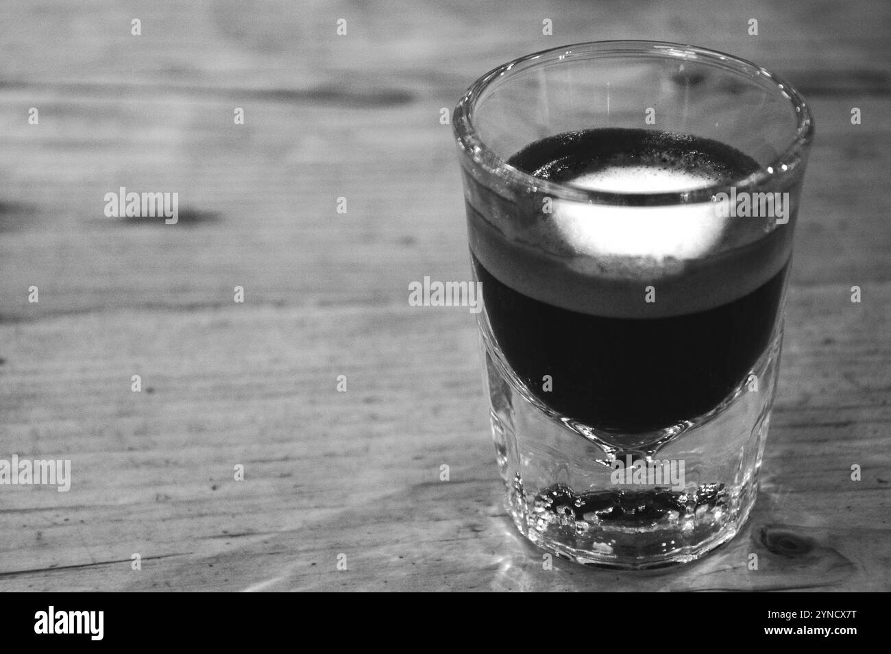 Starker Macchiato-Kaffee in kleinem Glas auf Holztisch. Reflexionen. Konzentriertes Konzept. Schwarzweißfoto. Stockfoto