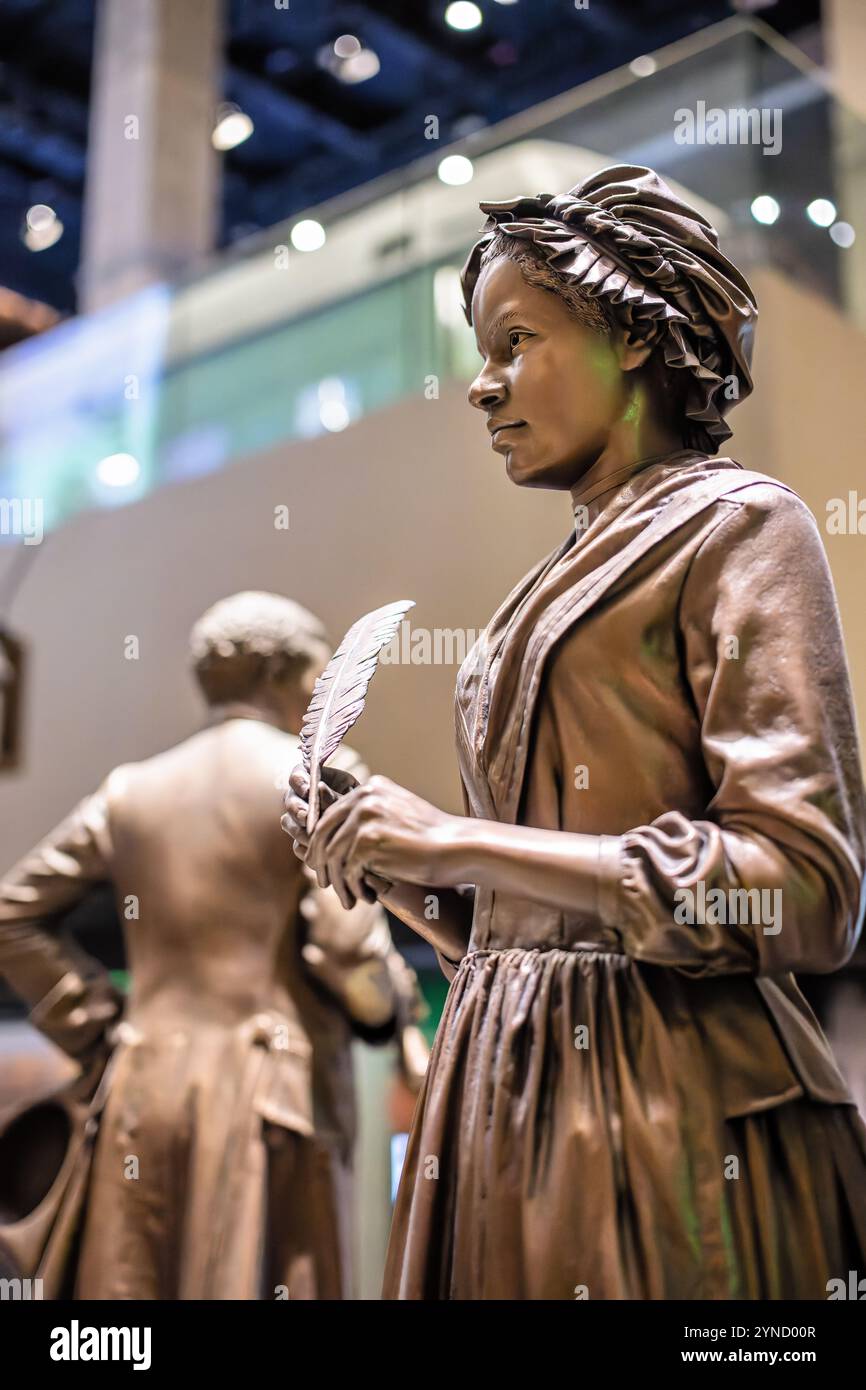 Phillis Wheatley Statue National Museum of African American History Washington DC // WASHINGTON DC – das National Museum of African American History and Culture präsentiert die Geschichte von Phillis Wheatley (1753–1784), Amerikas erstem afroamerikanischen Dichter. Wheatley wurde aus dem Senegal entführt und im Alter von sieben Jahren versklavt, beherrschte klassische Sprachen und wurde international bekannt für ihre 1773 erschienene Publikation Gedichte über verschiedene Themen, religiös und moralisch. Trotz ihrer literarischen Errungenschaften und ihrer Freiheit kämpfte sie während ihres gesamten Erwachsenenlebens mit Armut. Stockfoto