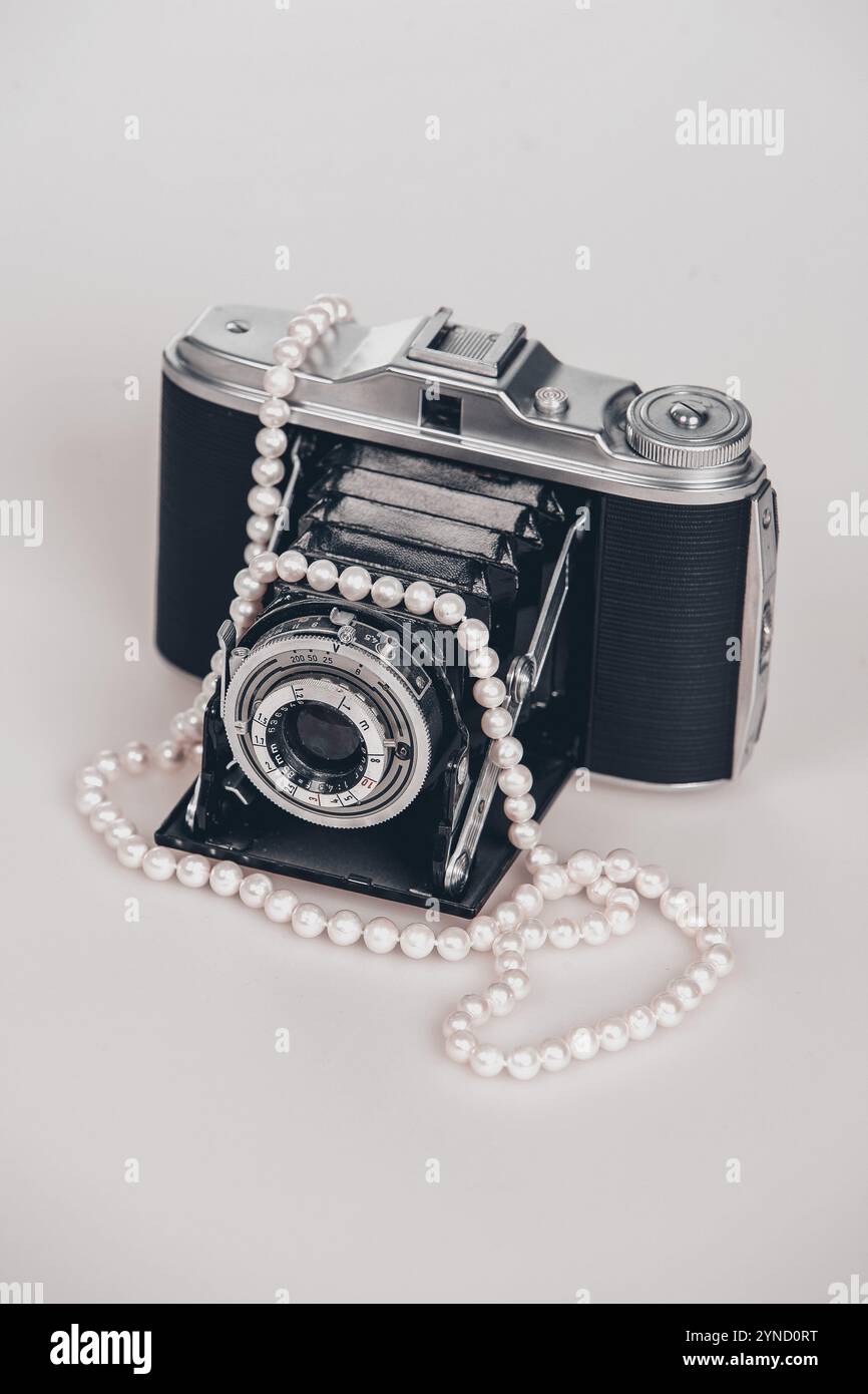 Alte Fotokamera mit einer Perlenkette drauf. Die Kamera ist schwarz und silber. Die Halskette ist weiß und hat Perlen. Stockfoto