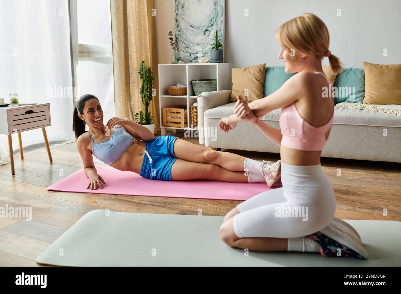 Zwei junge Frauen genießen ein lustiges Workout zu Hause und pflegen ihre Bindung durch Fitness. Stockfoto