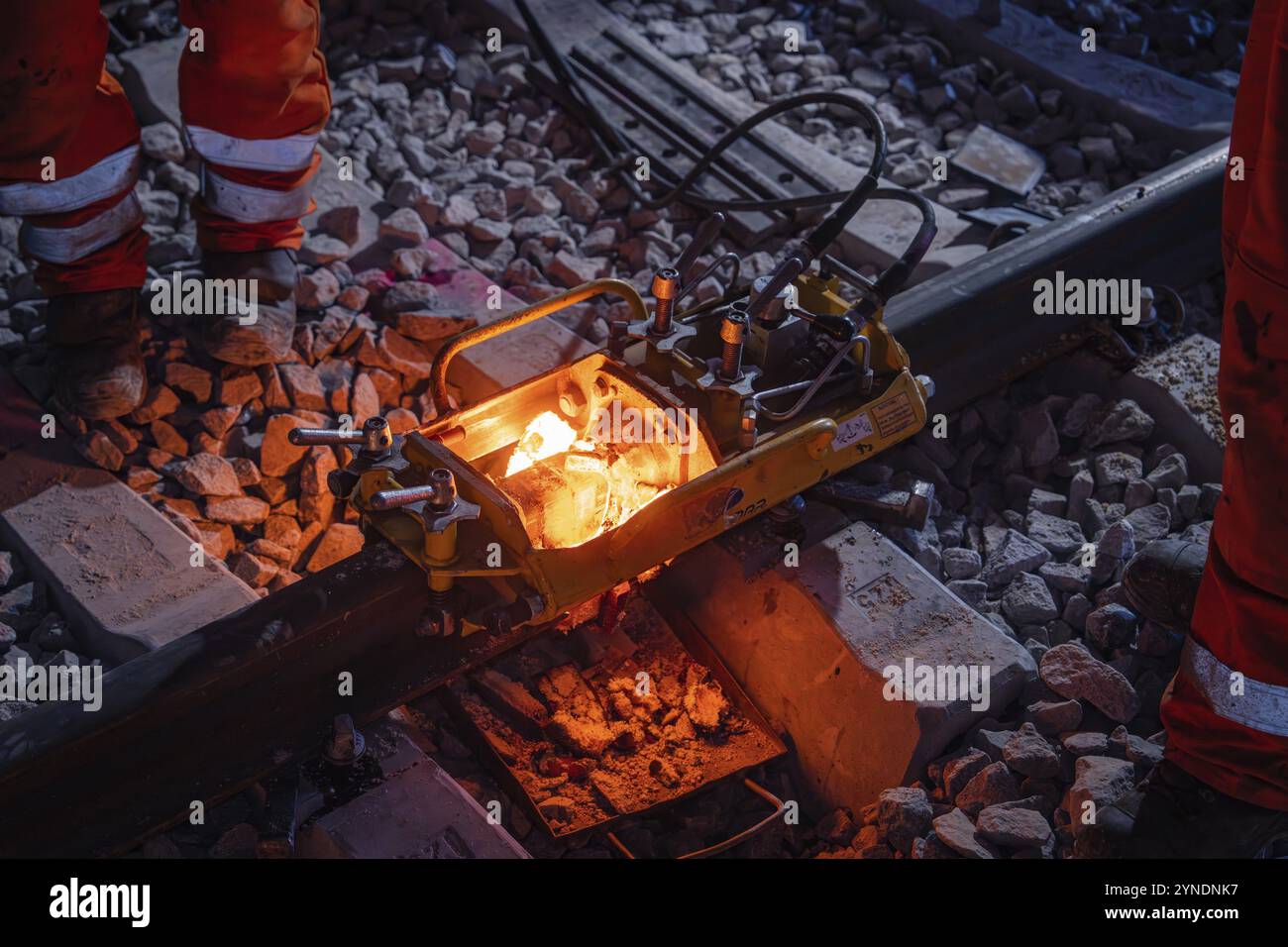 Arbeiter bei nächtlichen Gleisarbeiten mit Schweißgeräten und glühender Schmelzstelle auf den Schienen, Schienenschweißen, Gleisbau Hermann Hessebahn Stockfoto