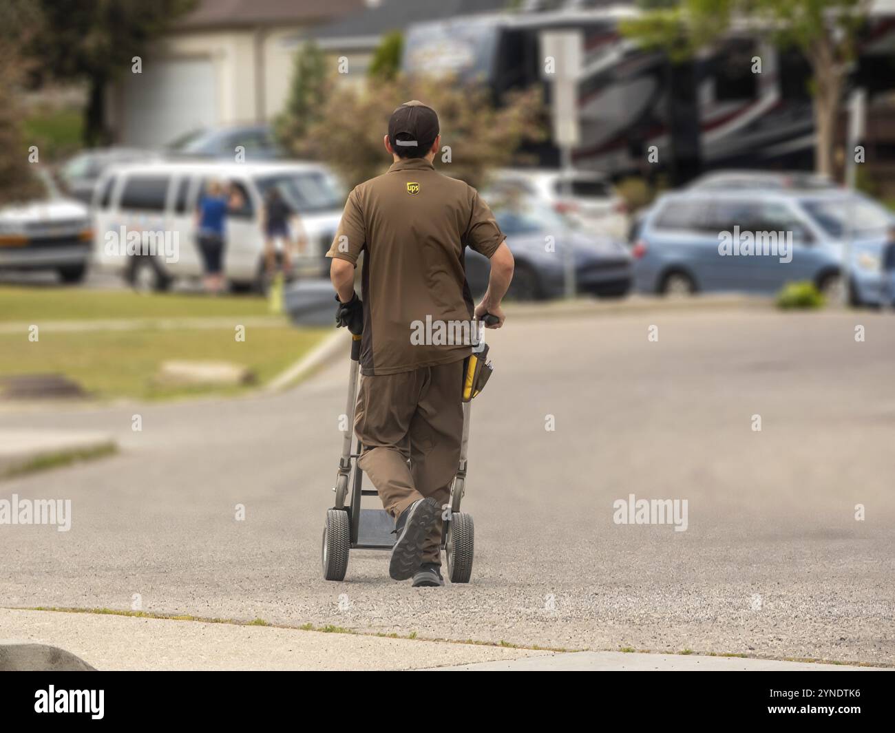 Calgary, Alberta, Kanada. August 2024. Ein UPS-Mitarbeiter in Uniform mit einem Handwagen auf der Straße Stockfoto