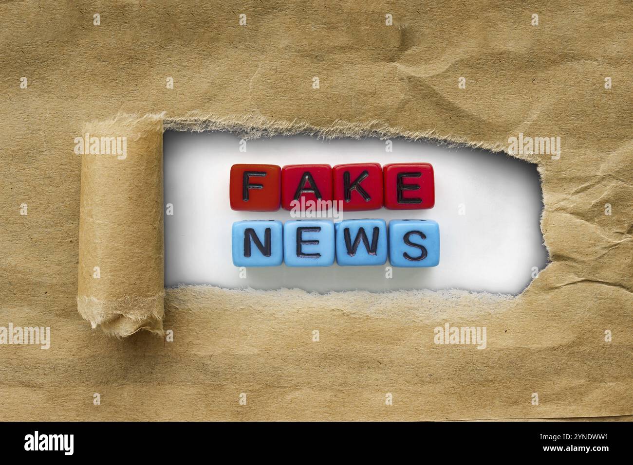 Braunes Paket Kraftpapier zerrissen, um rote & blaue Würfel mit den Worten zu enthüllen: Fake News. Concept Fake News Stockfoto