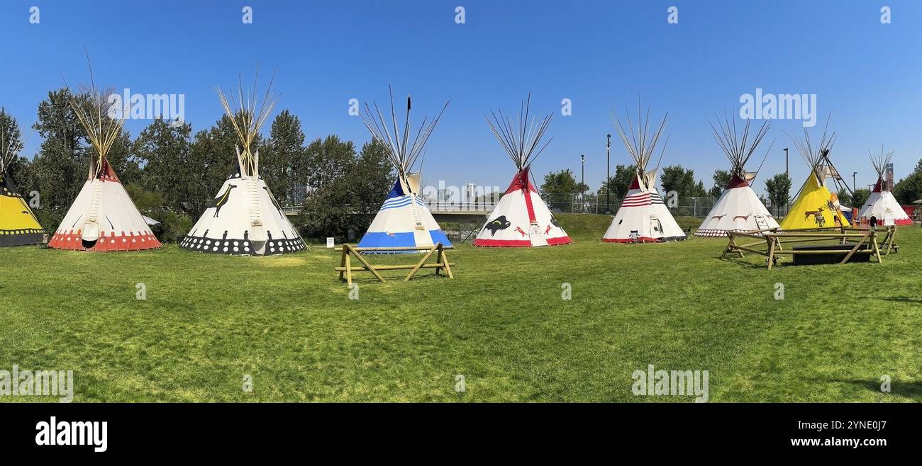 Calgary, Alberta, Kanada. Juli 2024. Eine Reihe farbenfroher Tipis steht auf einem grasbewachsenen Feld mit einer modernen Stadtlandschaft im Hintergrund Stockfoto