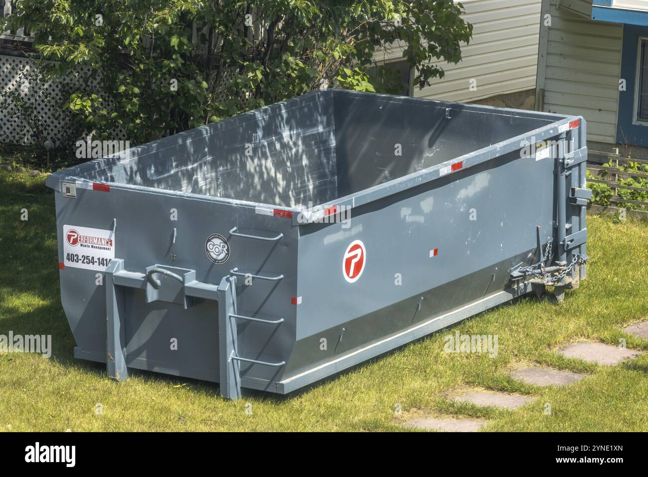 Calgary, Alberta, Kanada. August 2024. Ein großer, leerer Müllcontainer auf einem Rasen. Der Müllcontainer ist sauber und grau, mit roten und weißen Abzweigungen Stockfoto