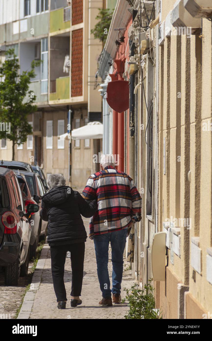 Zwei ältere Menschen, die den Rücken abgewandt haben, gehen die Straße hinunter, wo ihre Gesichter nicht zu sehen sind, wie sie Hände in einer Szene der Liebe und des Aff halten Stockfoto