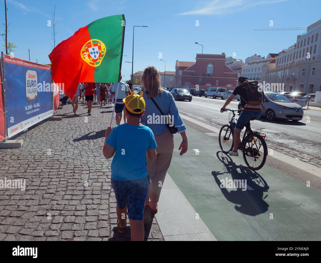 Lissabon, Portugal - Junge, der die portugiesische Flagge hält, geht auf der Straße. Leute, die das UEFA-Euro-Fußballspiel in Doca da Marinha sehen Stockfoto