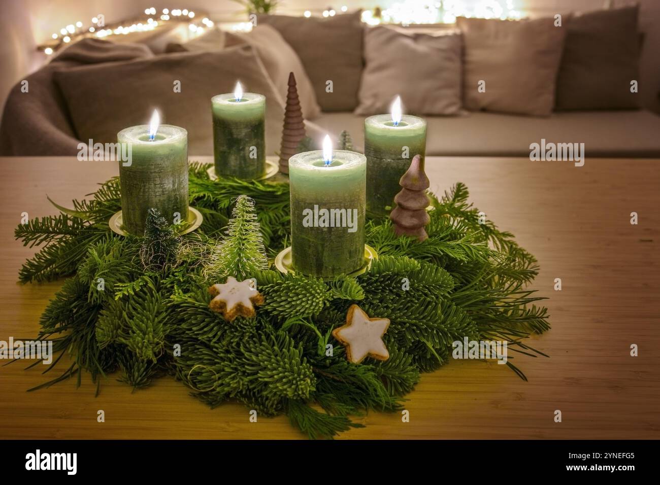 Vierter Adventskranz mit vier leuchtenden grünen Kerzen und Weihnachtsdekoration auf einem Holztisch im Wohnzimmer, Kopierraum, ausgewählter Fokus, schmal de Stockfoto