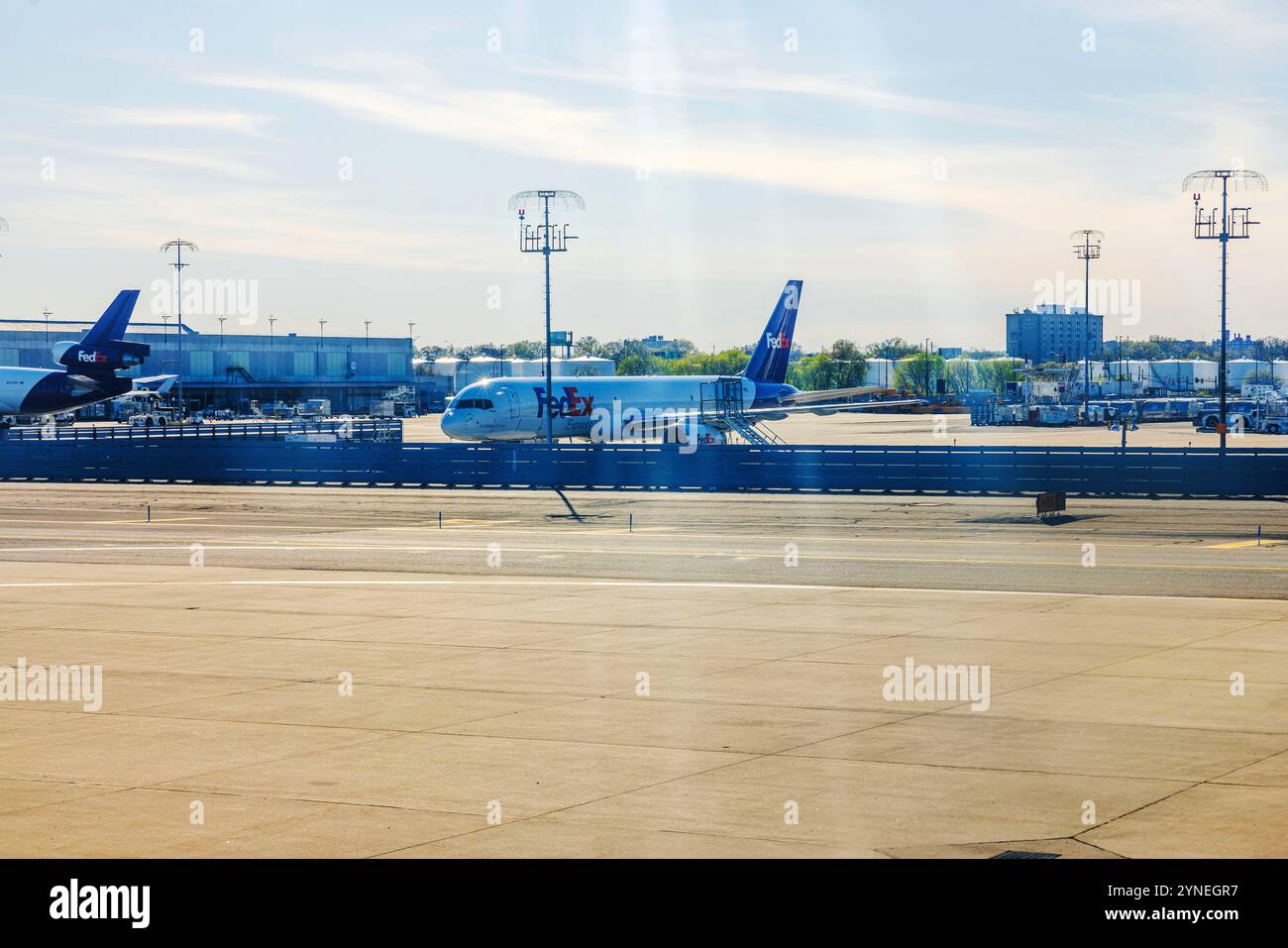 FedEx Frachtflugzeuge parkten am Flughafenterminal unter hellem sonnigem Himmel mit Ladegeräten und Gebäuden im Hintergrund. New Jersey, USA. Stockfoto