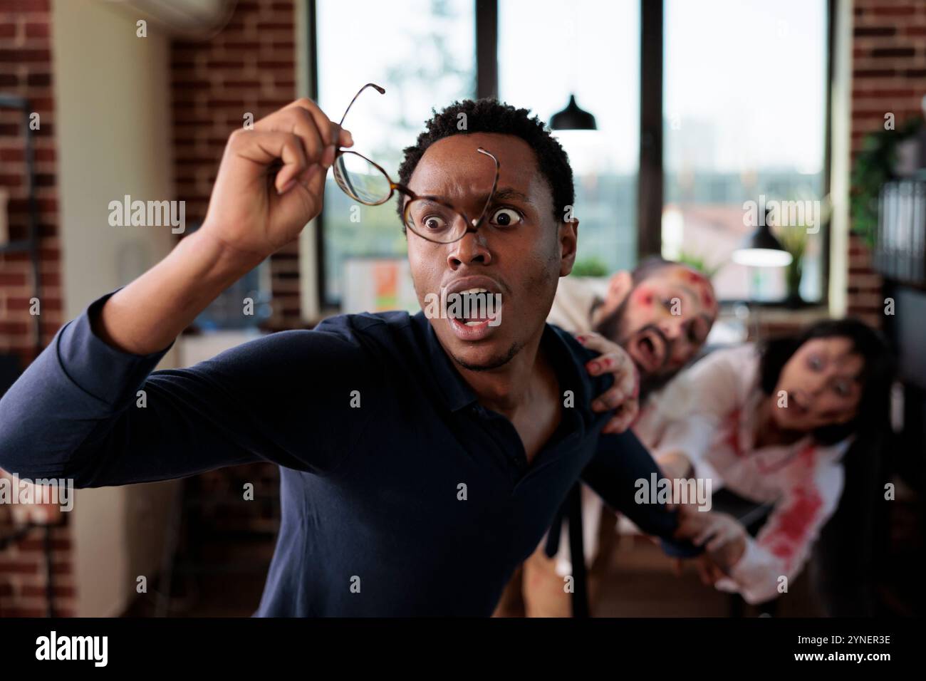 Schauspieler, die Zombies in der Horrorfilmszene spielen, jagen afroamerikanischen Geschäftsmännern, die Brillen ablegen. Mann und Frau mit wilden übernatürlichen Kreaturen Rollen in Thriller-Film Fight Worker am Büroset Stockfoto