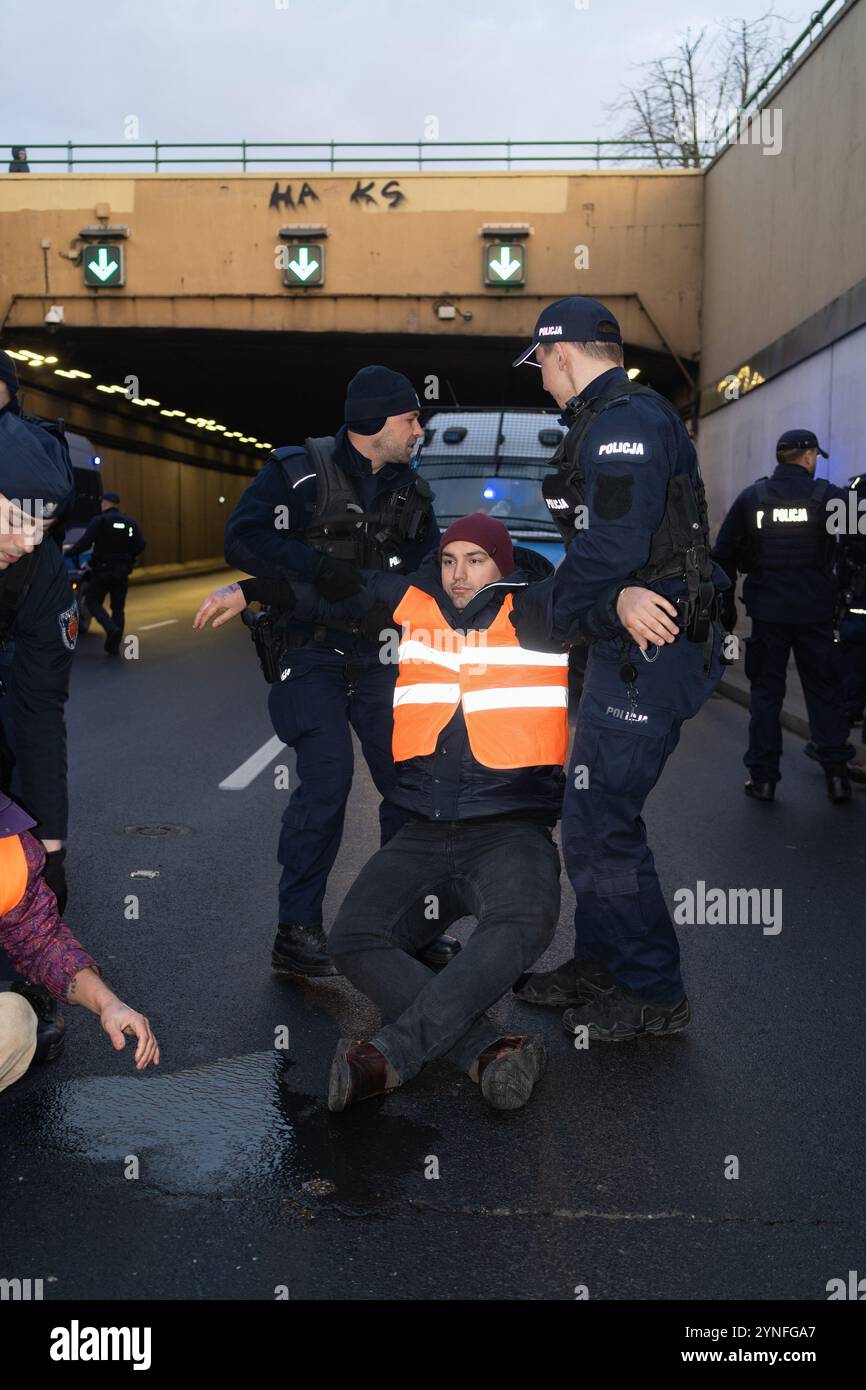 Polizisten entfernen während der Demonstration einen Demonstranten von der Straße. (Ostatnie Pokolenie/letzte Generation) initiierte eine Reihe von Blockaden auf der Wislostrada, um die Klimapolitik der Regierung unter Donald Tusk in Frage zu stellen. Gegen 7:00 Uhr morgens blockierten ein Dutzend Aktivisten in orangefarbenen Westen den Verkehr in der Nähe des Tunneleingangs. Sie trugen Banner, darunter eines mit der Aufschrift „Tusk treibt den Klimakollaps an“. Die Gruppe kündigte eine wöchentliche Rückkehr an, um Wislostrada als Symbol für anhaltenden zivilen Widerstand zu etablieren. Stockfoto