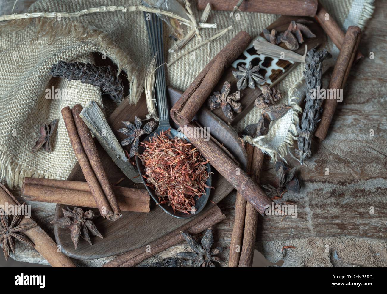 Saflor auf Löffel mit Zimt, Sternanis und getrockneter Prunella vulgaris (Xia ku cao) auf altem rustikalem Holzhintergrund. Verschiedene Gewürze und Naturkräuter Stockfoto