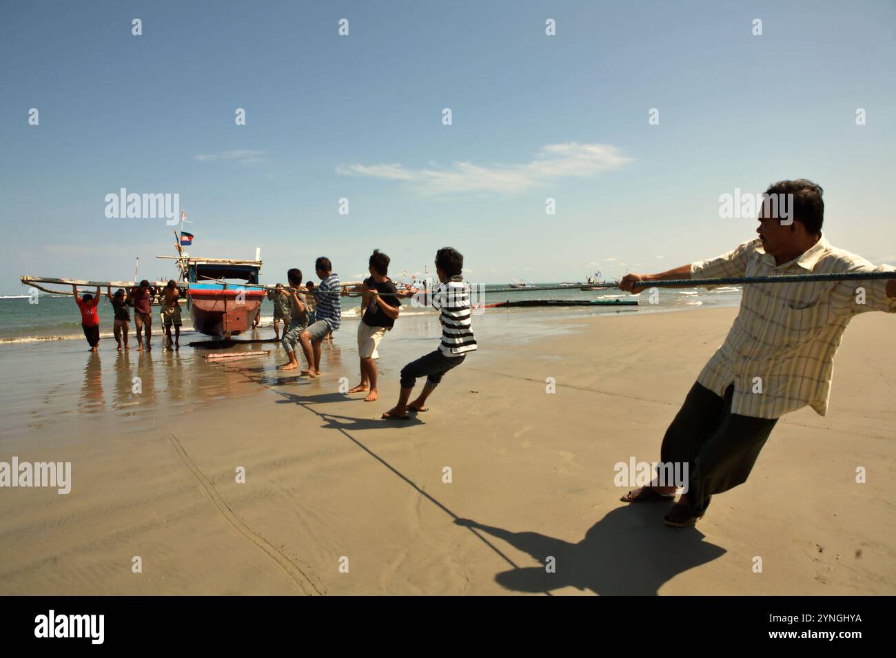 Männer schieben und ziehen ein Fischerboot mit einem Seil am Malabero (Malabro) Strand, im Hintergrund des Indischen Ozeans, in Bengkulu, Indonesien. Stockfoto