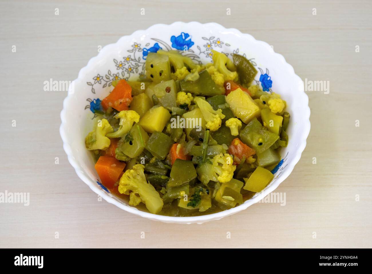 Gesundes Gemüse Curry in einer weißen Keramikschale auf einer Holzoberfläche, mit einer Vielzahl von gemischtem Gemüse einschließlich Blumenkohl, Karotten, Bohnen, s Stockfoto