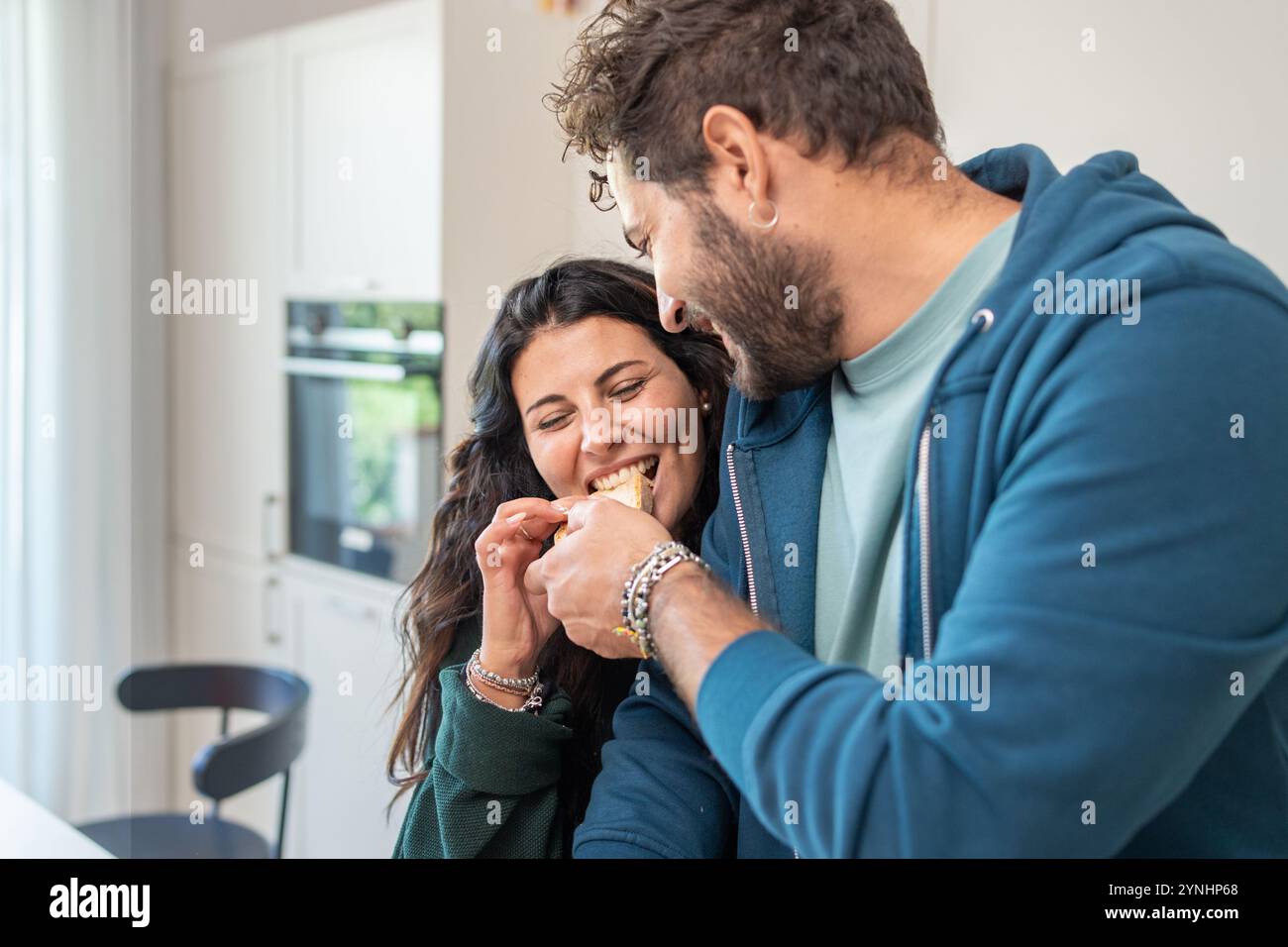Natürliche Interaktion zwischen Partnern, die hausgemachte Speisen in der modernen Küche genießen. Echte emotionale Verbindung, die während des täglichen Kochens der Mutter festgehalten wird Stockfoto