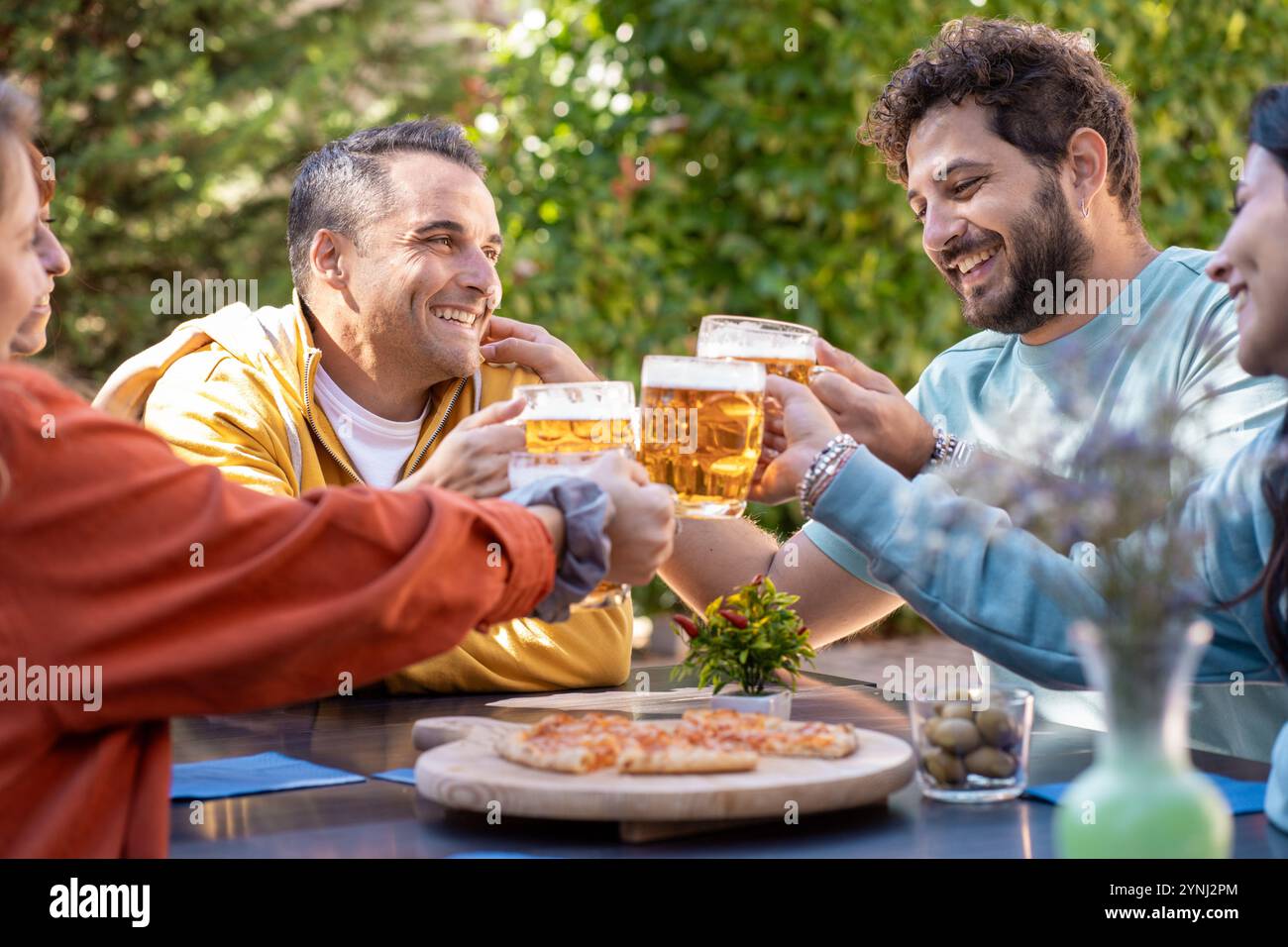 Spontaner Moment, in dem Freunde während des Abendessens im Freien lebhafte Gespräche genießen. Natürliche Ausdrucksformen von Freude und Freundschaft im Garten Stockfoto