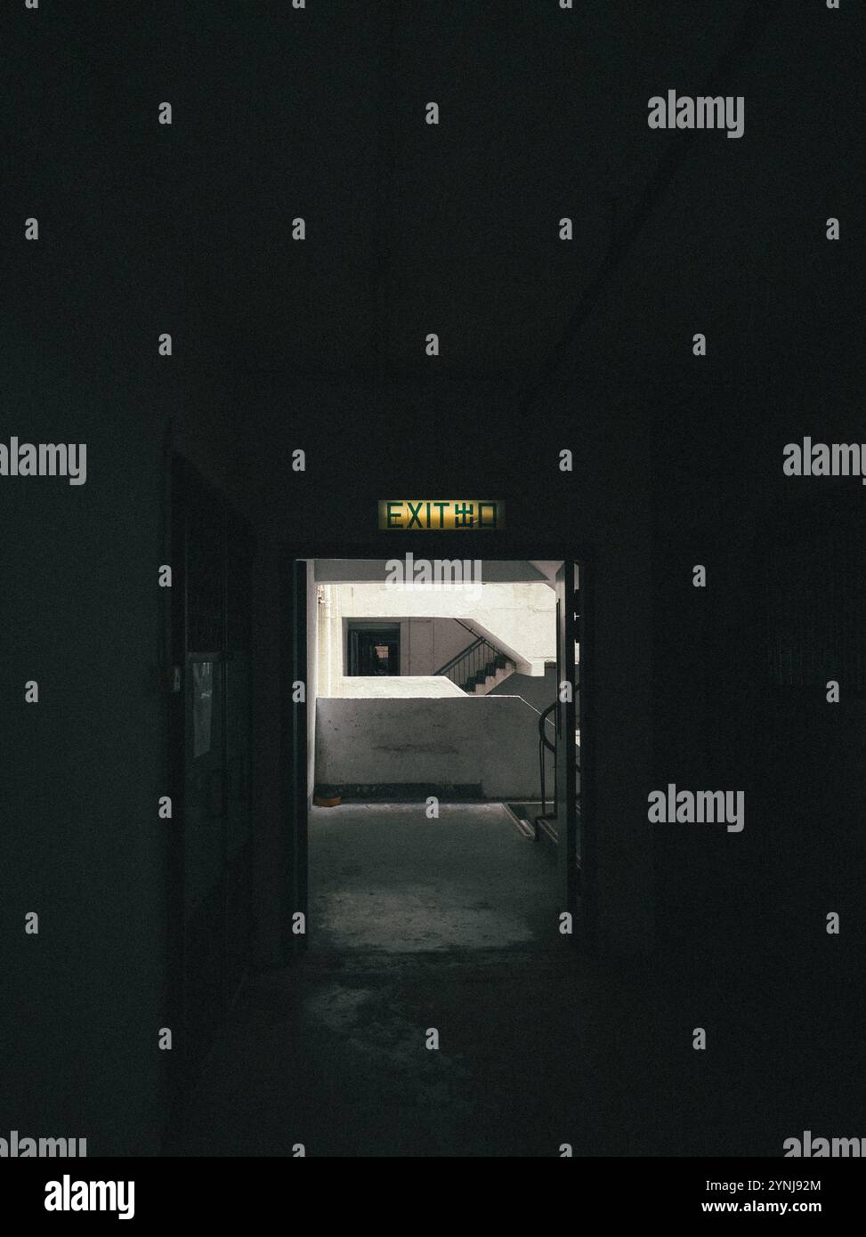 Schwach beleuchtete Eingangstür führt zur Außentreppe in einem städtischen Gebäude mit dramatischen Schatten Stockfoto