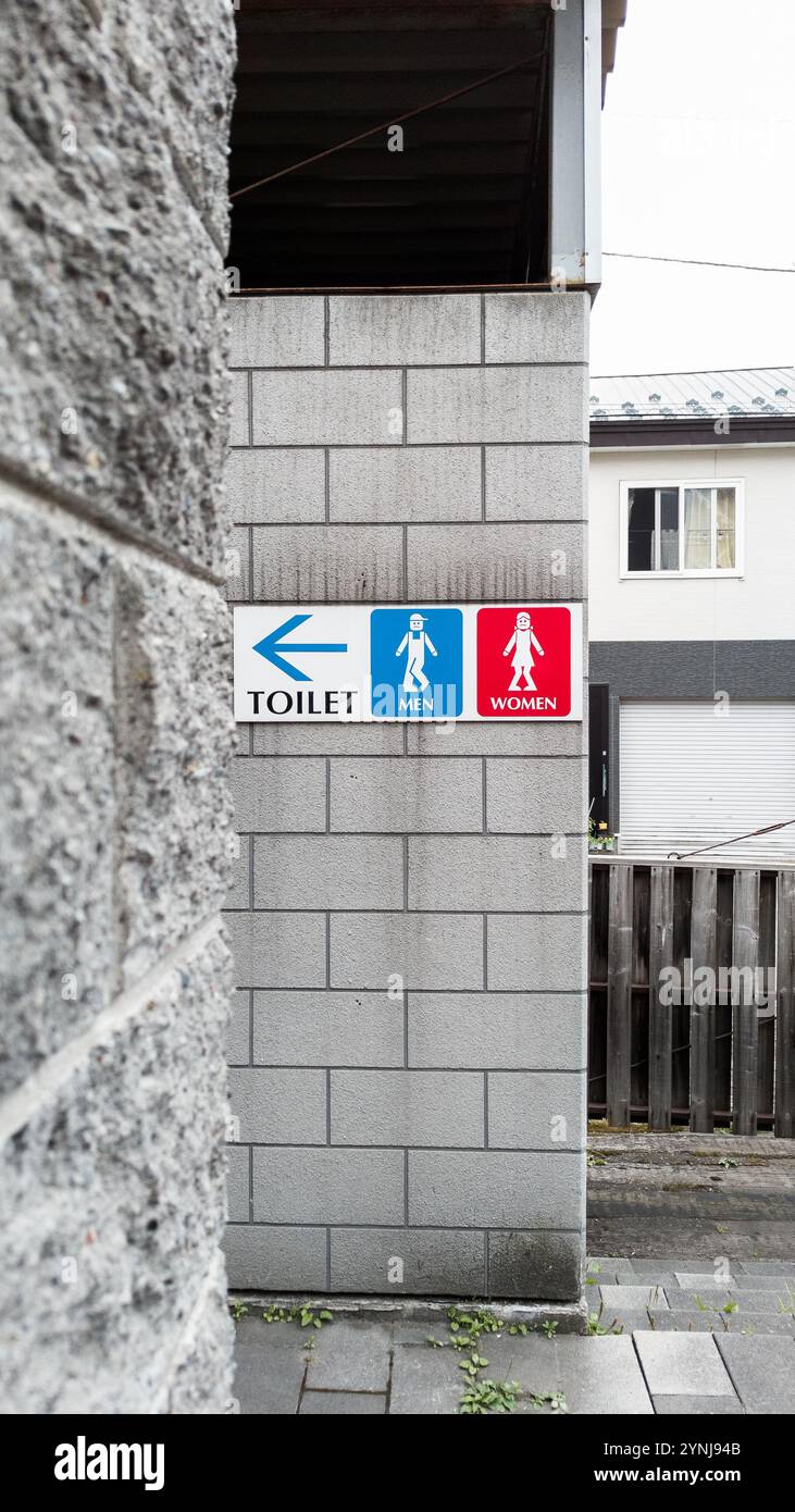 Richtungsschild für öffentliche Toiletten mit humorvollen Gender-Symbolen an der Betonmauer in urbanem Ambiente Stockfoto