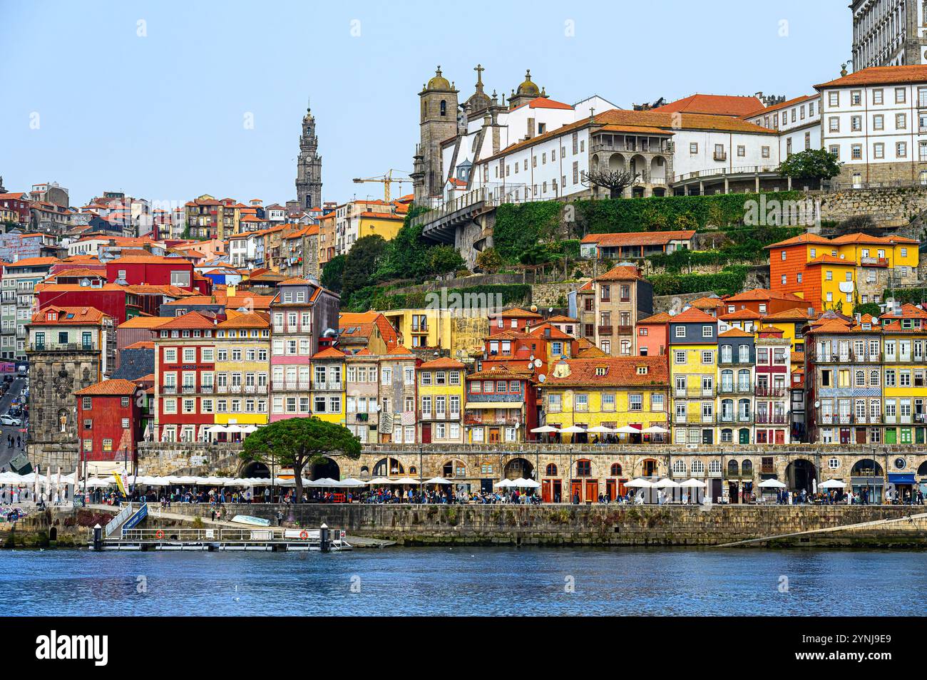 Porto, Portugal - 17. Juli 2024: Fassade von pastellfarbenen Gebäuden im Flussviertel mit dem Turm der Clerigos-Kirche in der Ferne. Stockfoto