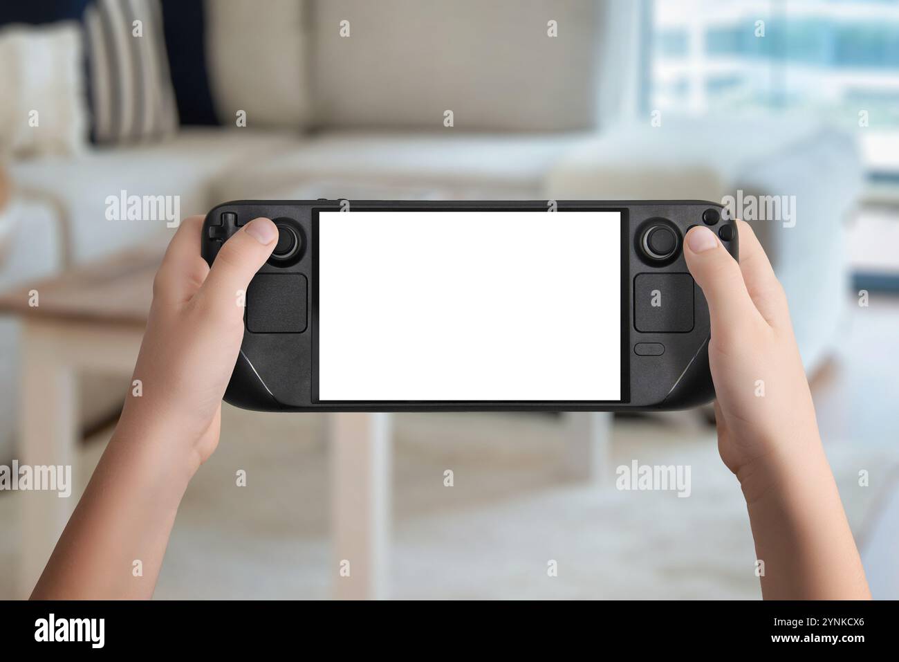 Flache Lay- oder Vorderansicht der Hände, die eine schwarze Handspielkonsole mit isoliertem Bildschirm halten, gemütlicher Hintergrund im Wohnzimmer, ideal für Mockup-Spiele Stockfoto