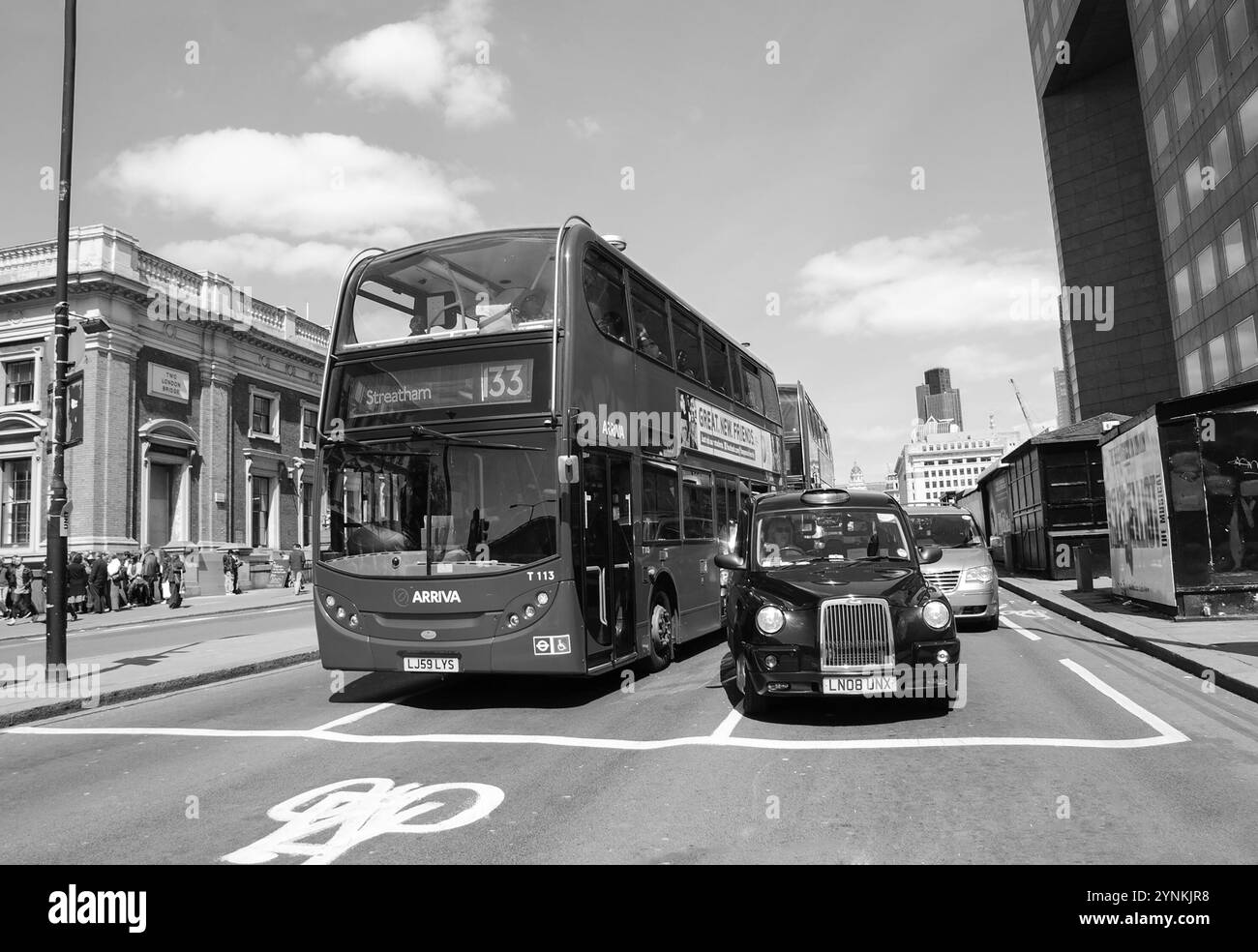 LONDON, ENGLAND, Großbritannien - 3. MAI 2014: Roter Doppeldeckerbus und traditionelles Taxi stehen an einer Ampel hinter der ASL (Advanced Stop Line). Schwarzweiß Stockfoto