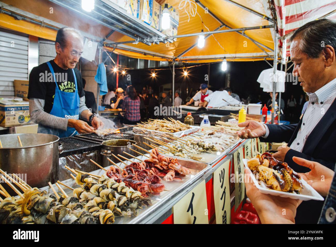 Tokio, Japan - 26. November 2024 : lokales japanisches Streetfood auf dem Nachtmarkt in Tokio, Japan. Mann, der Yakitori auf dem Straßenmarkt grillt. Stockfoto