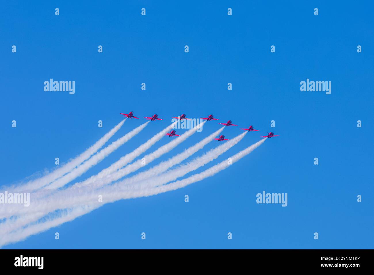 Die legendären Roten Pfeile führen einen beeindruckenden Formationsflug durch und zeigen außergewöhnliche Präzision und Geschicklichkeit. Vor einem leuchtend blauen Himmel, ihrem roten Jet Stockfoto