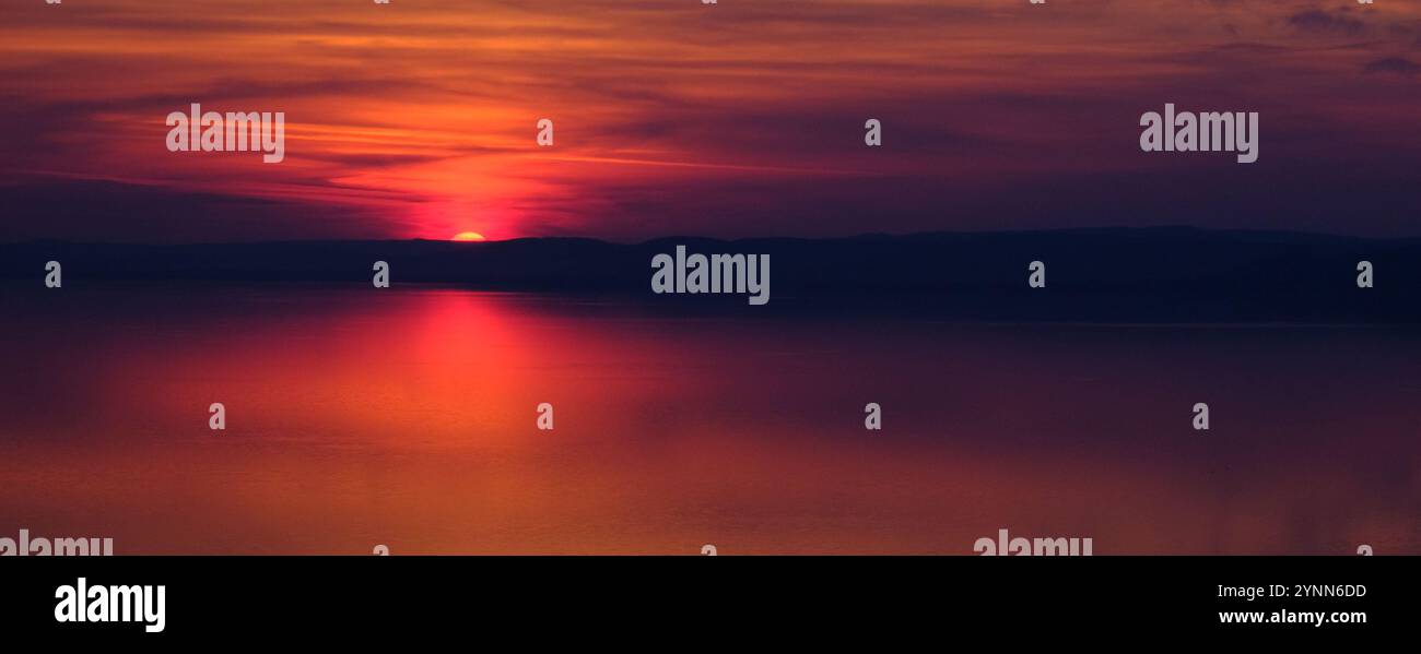 Atemberaubender Sonnenuntergang über einem ruhigen Balaton-See mit leuchtenden Rot- und Lila-Tönen, die den Himmel erleuchten und sich auf der ruhigen Wasseroberfläche spiegeln Stockfoto