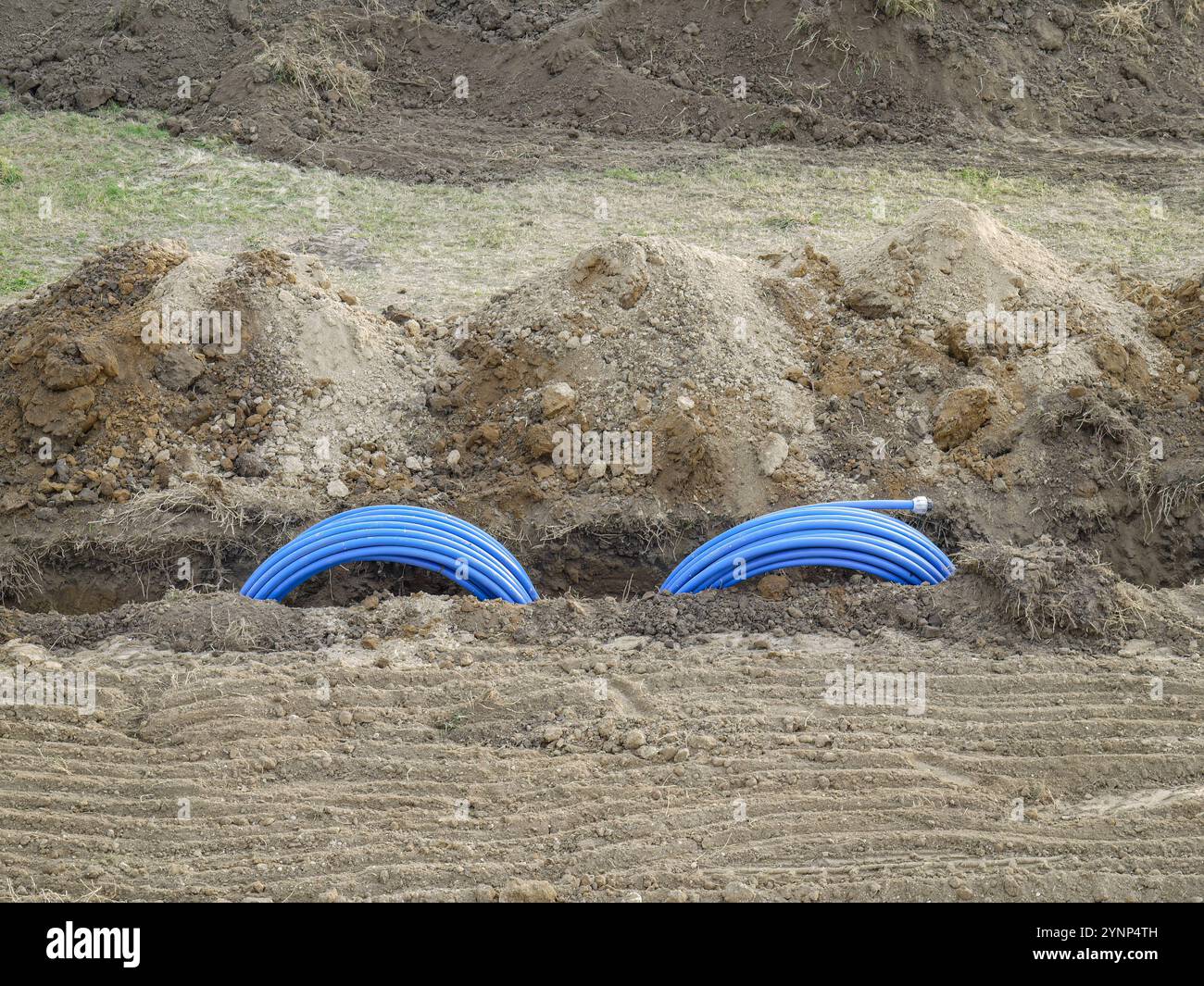Blaue Rohre des Erdkollektors der Wärmepumpe werden auf einer Baustelle positioniert, die für die Untertage-Installation bereit ist. Die Szene zeigt Aspekte des civ Stockfoto