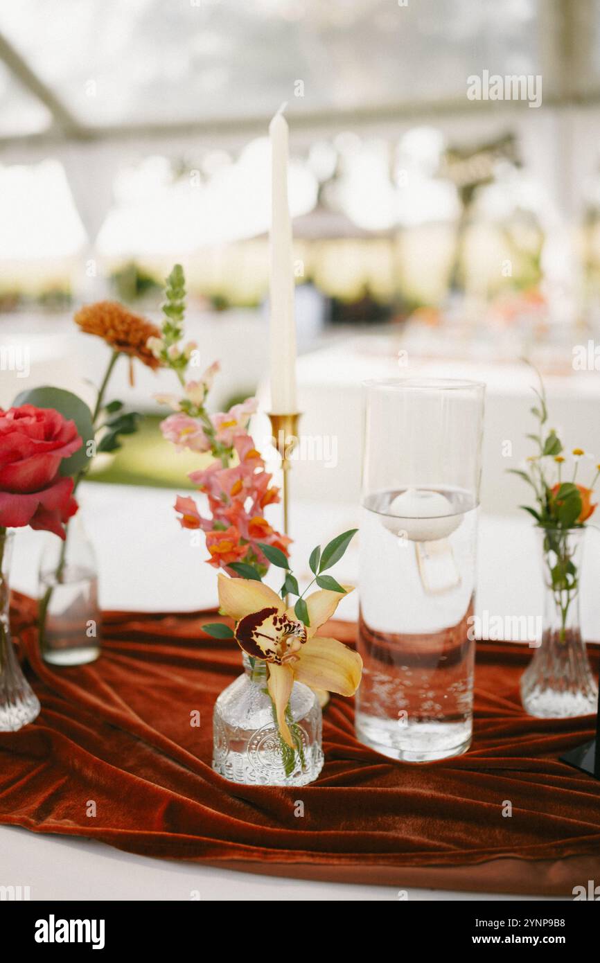 Elegante Einrichtung im Hinterhof mit farbenfrohen Herbstblumen, Messing-Kerzenleuchtern und einer Tischläufer aus Terrakotta-Samt. Stockfoto