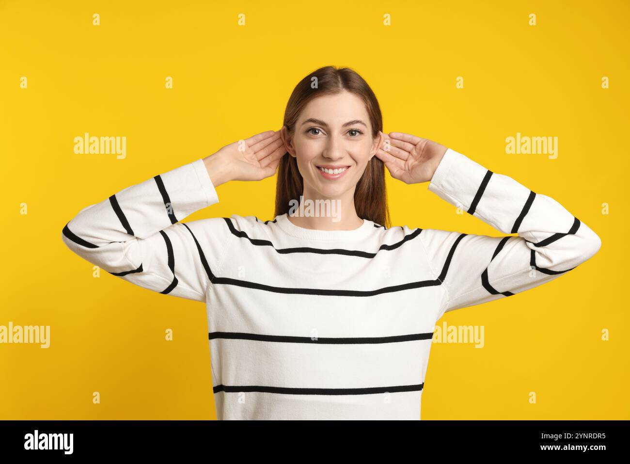 Frau zeigt Hand-Ohr-Geste auf dunkelgelbem Hintergrund Stockfoto