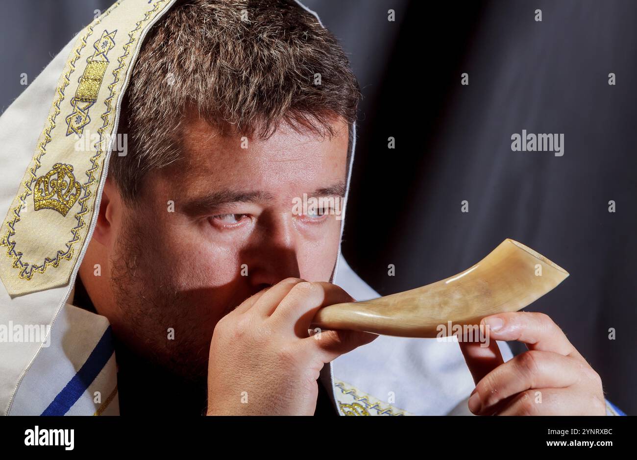 Ein Mann, der in zeremoniellen Schal gekleidet ist, bläst Schofar, traditionelles Horn und ruft während des jüdischen religiösen Ereignisses eine heilige Atmosphäre hervor. Stockfoto