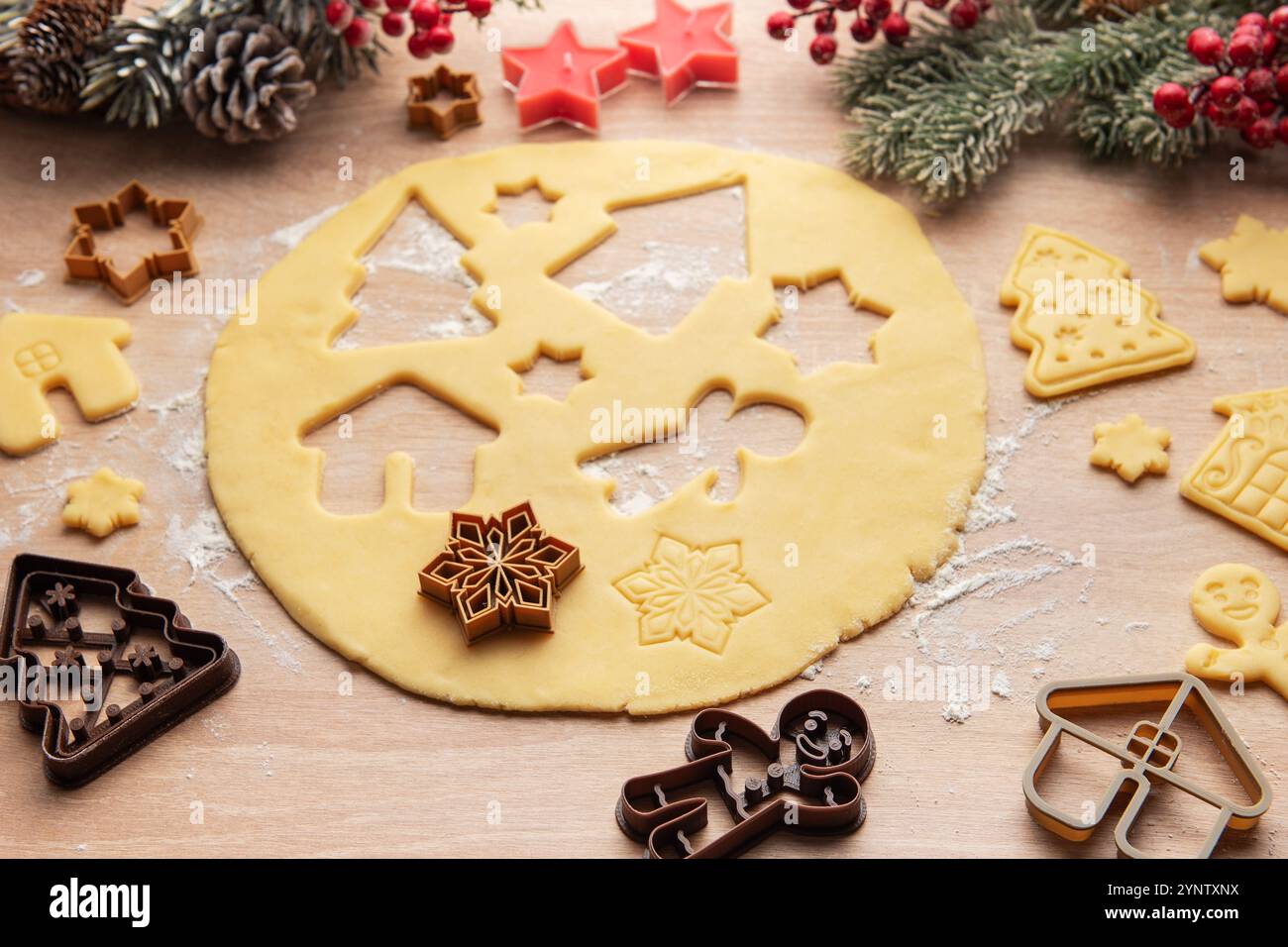 Ausgerollter Teig wird für weihnachtskekse zubereitet, mit verschiedenen festlichen Formen wie Häusern, Bäumen, Sternen und Schneeflocken Stockfoto