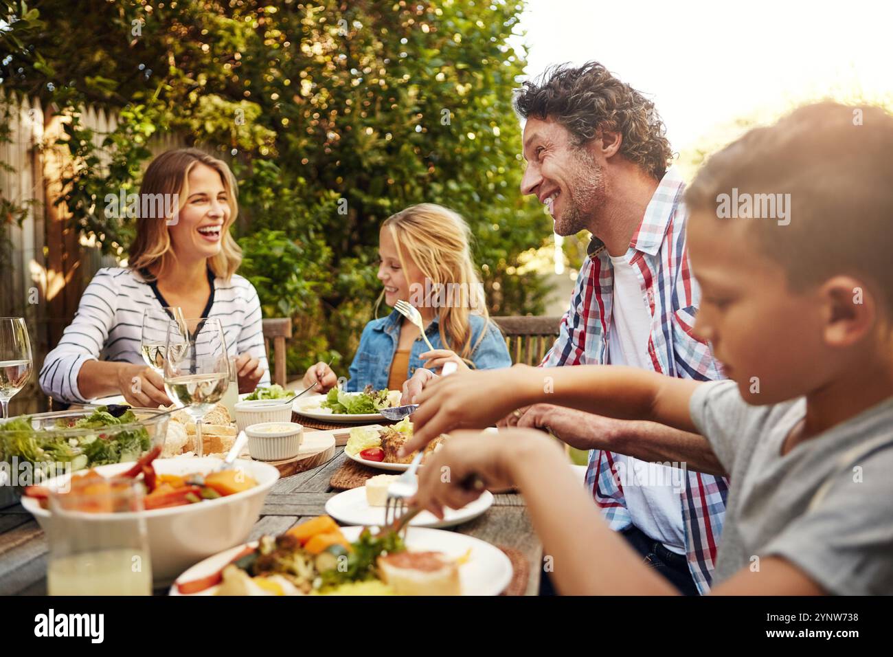 Mom, Dad und glückliche Kinder beim Mittagessen im Freien mit einem Lächeln, Feiern und Familienessen zusammen im Garten. Vater, Mutter und Kinder am Tisch Stockfoto
