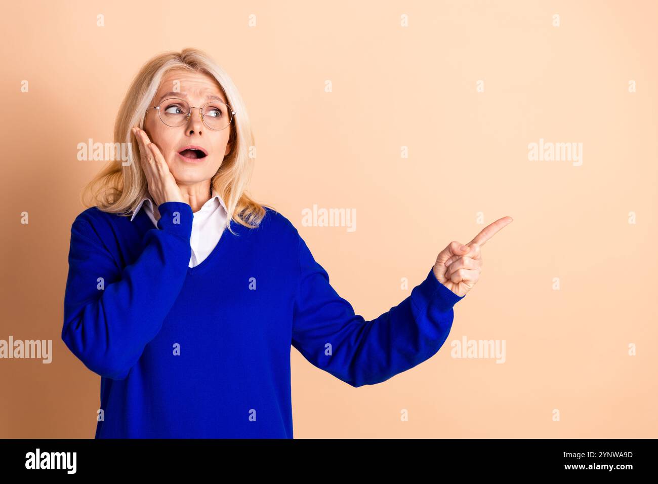 Stilvolle reife Frau in blauem Pullover, die eine ausdrucksstarke Geste vor beigefarbenem Hintergrund macht Stockfoto
