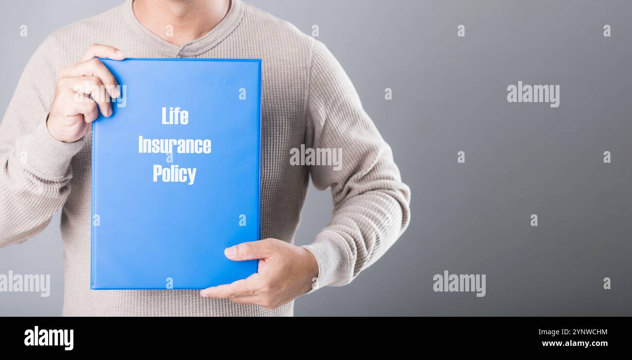 Man hält ein blaues Heft für Lebensversicherungen vor grauem Hintergrund, das die Bedeutung der Planung und Sicherung finanzieller Absicherung symbolisiert Stockfoto