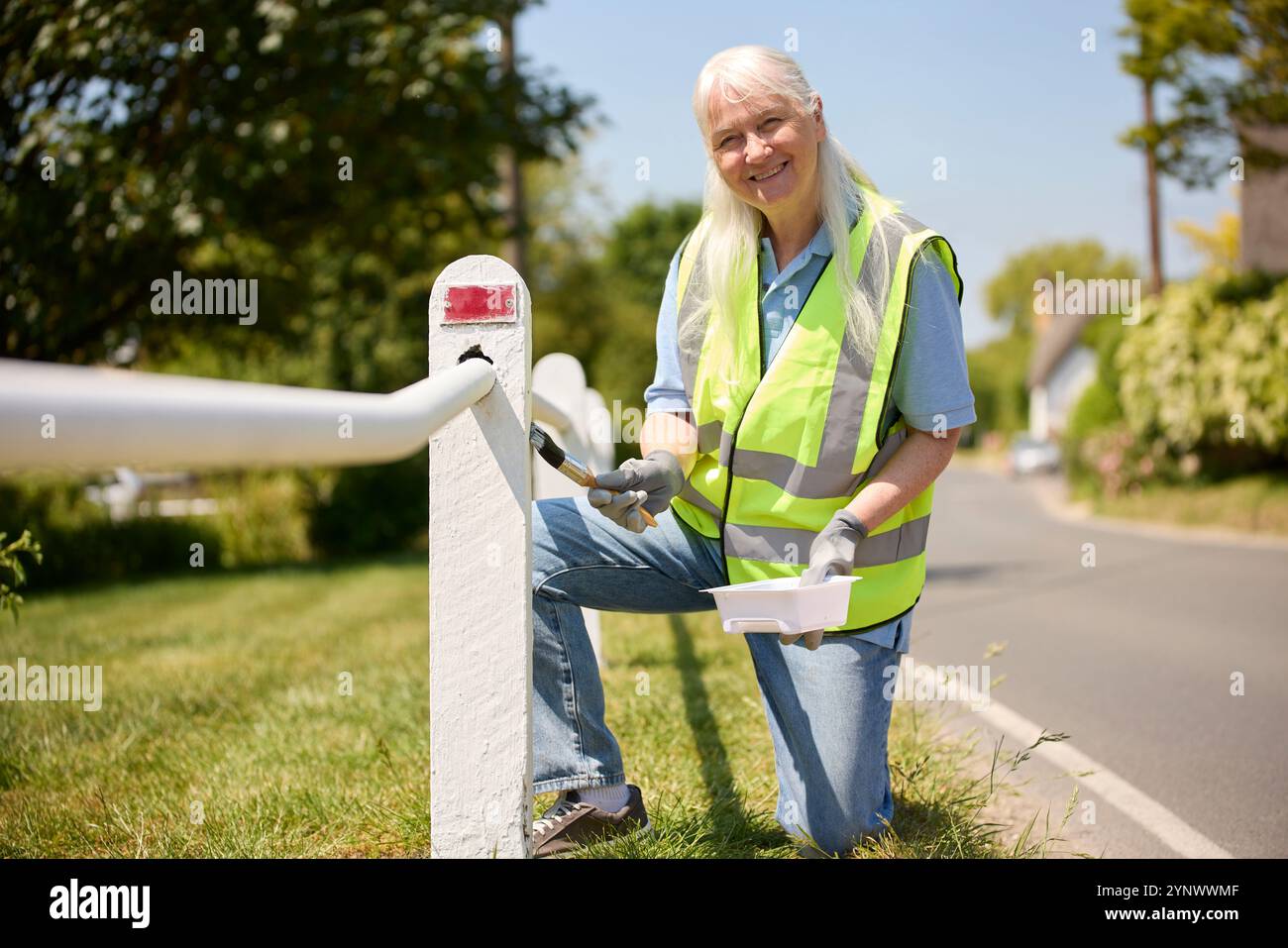 Seniorin Im Ruhestand, Die Durch Die Painting Fence Post Zur Erhaltung Der Gemeinde Beiträgt Stockfoto