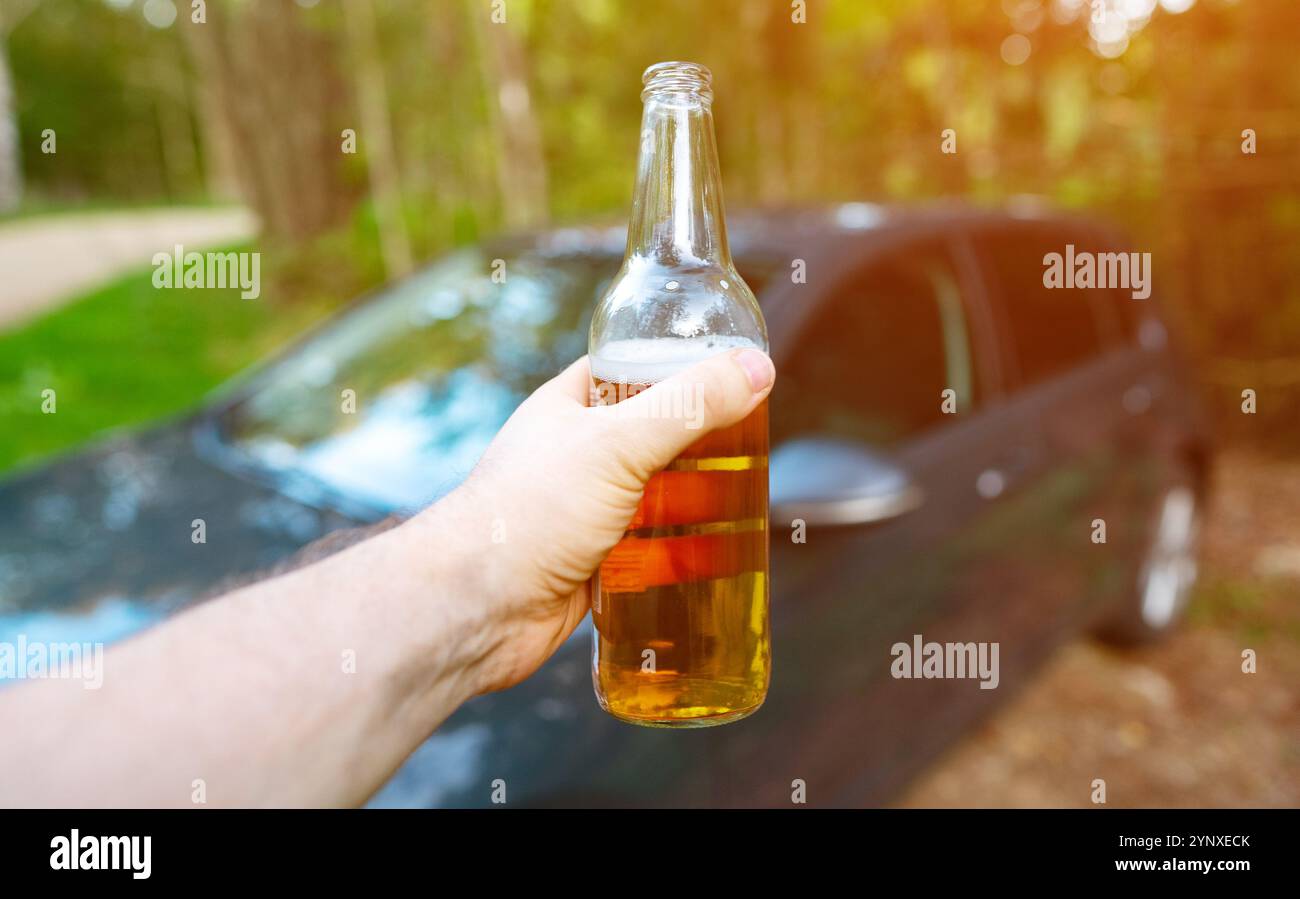 Ein Mann mit einer Flasche Bier steigt in ein Auto. Betrunkenes Fahrkonzept. Stockfoto