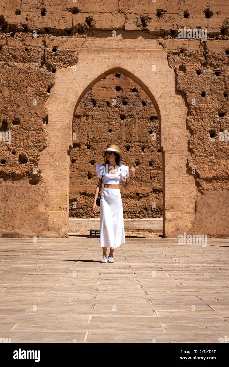 Junge dunkelhaarige Frau in weißem Kleid und Hut posiert im Innenhof des El Badii Palace Marrakesch, Marokko Stockfoto