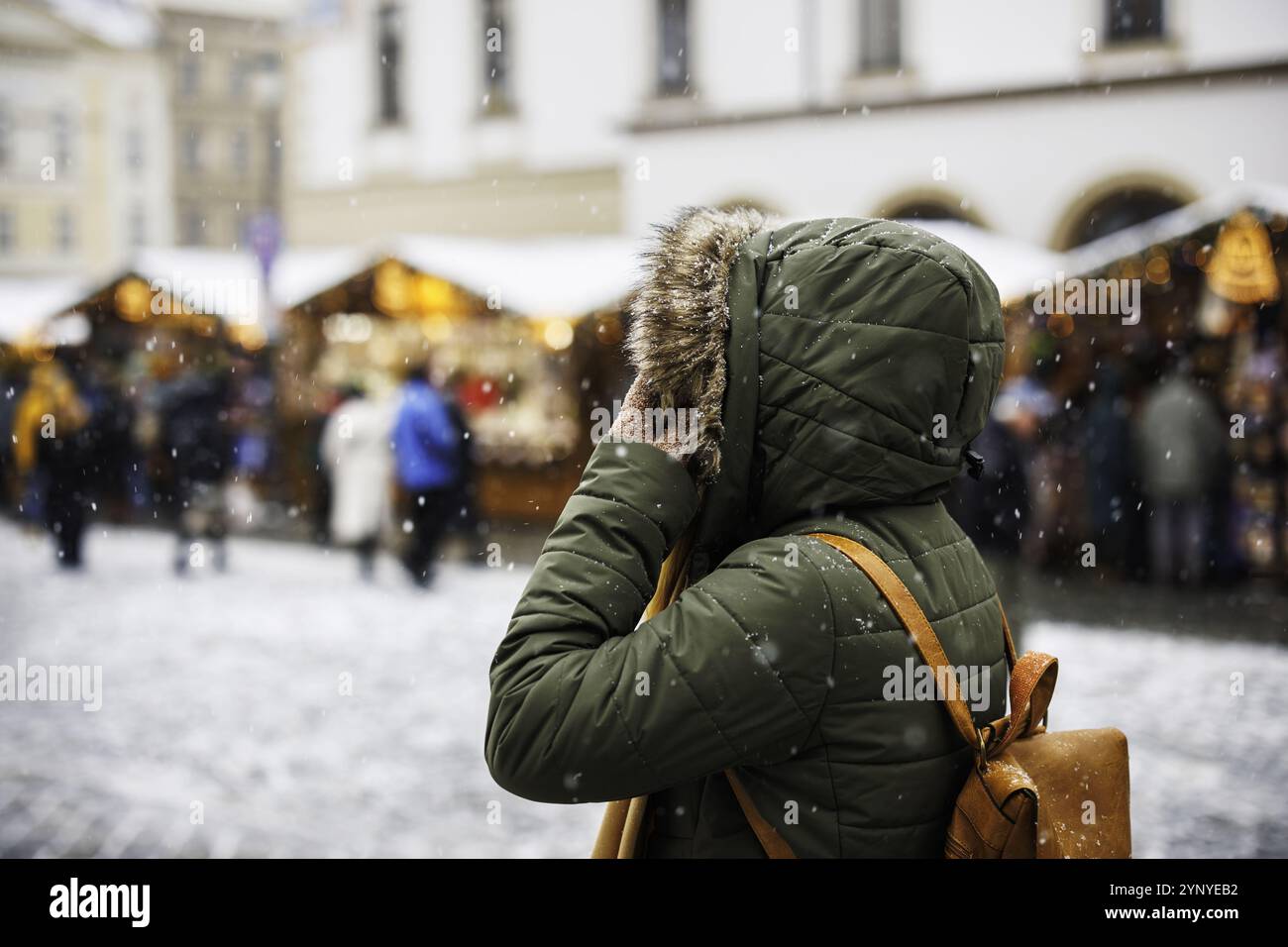 Frau läuft während der Adventsferien zum Weihnachtsmarkt auf dem Stadtplatz. Im Winter schneit es in der Stadt. Weihnachtsfest Stockfoto