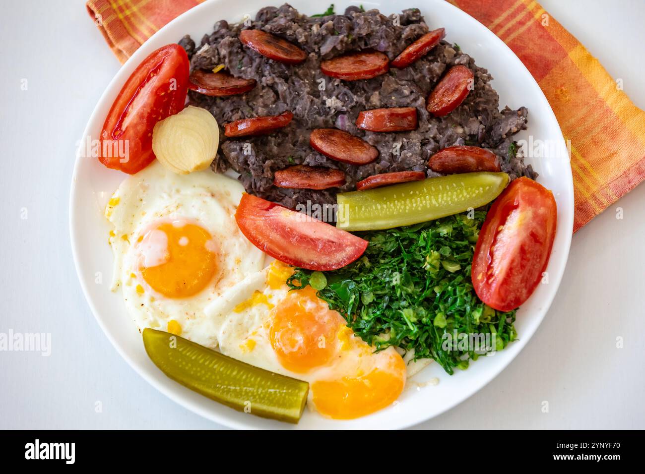 Rustikales, nahrhaftes brasilianisches Essen, Eintopf aus schwarzen Bohnen mit Eiern, gegrillte Würstchen, Gurken und natürliche Gärung, Grünkohl und Gemüse. Echtes Essen Stockfoto