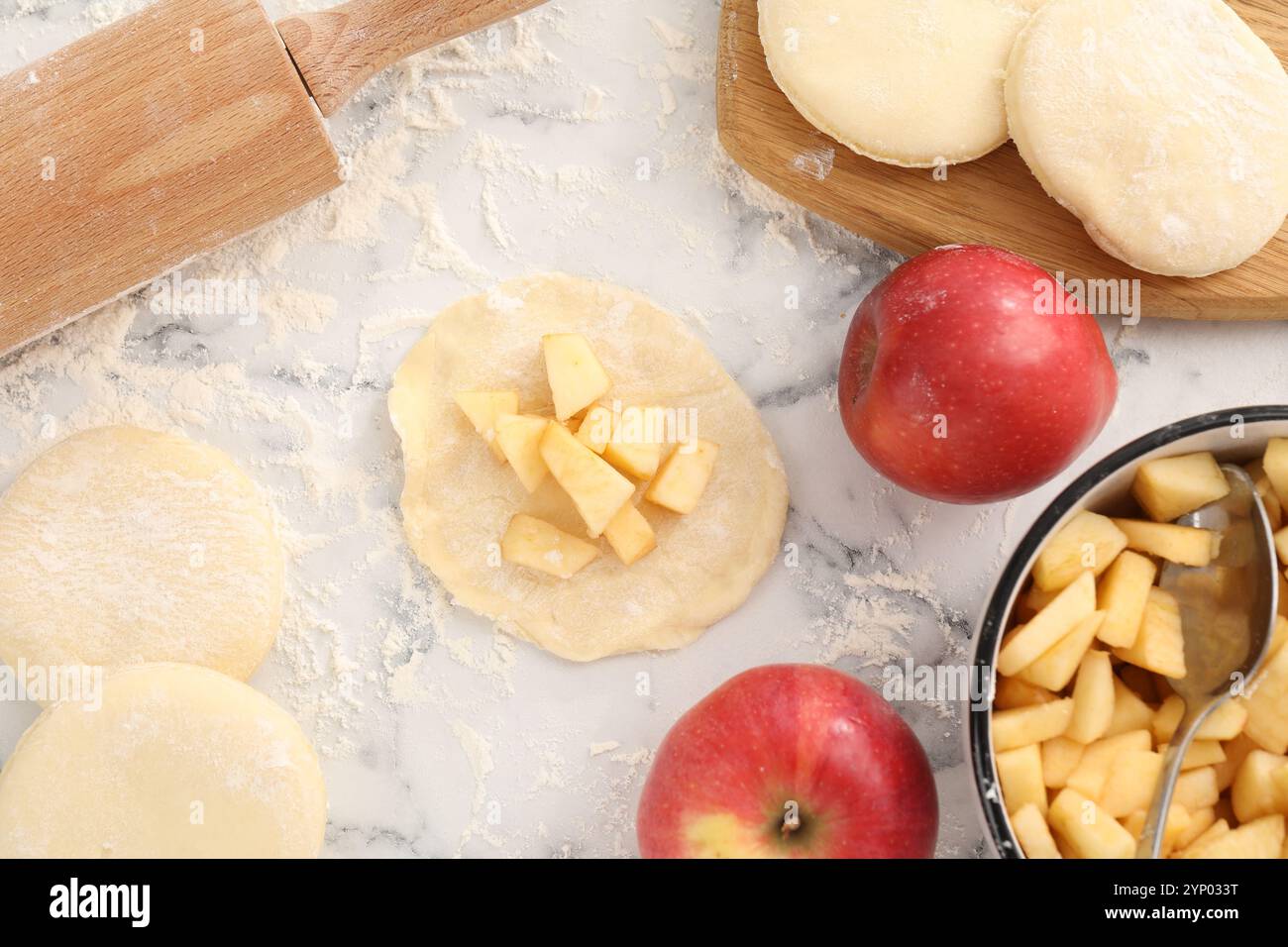 Pirozhki (gefüllte Teigtaschen). Teigstücke mit Äpfeln auf weißem Marmortisch, flach gelegt Stockfoto Pirozhki (gefüllte Teigtaschen). Teigstücke mit Äpfeln auf weißem Marmortisch, flach gelegt Stockfoto