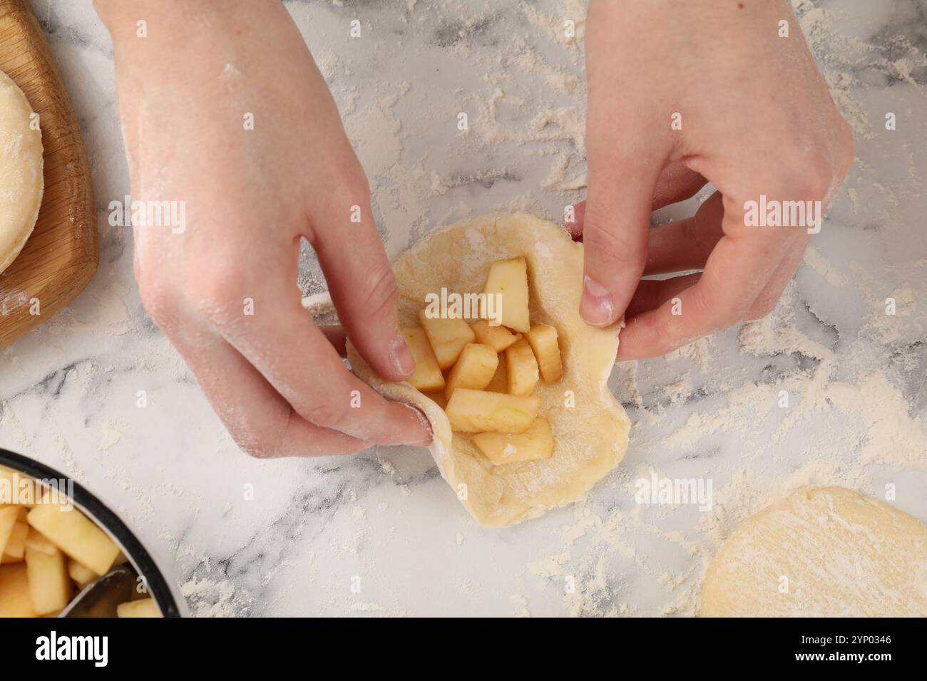 Frau, die Pirozhki (gefüllte Kuchen) mit Äpfeln an weißem Marmortisch herstellt, Blick von oben Stockfoto Frau, die Pirozhki (gefüllte Kuchen) mit Äpfeln an weißem Marmortisch herstellt, Blick von oben Stockfoto