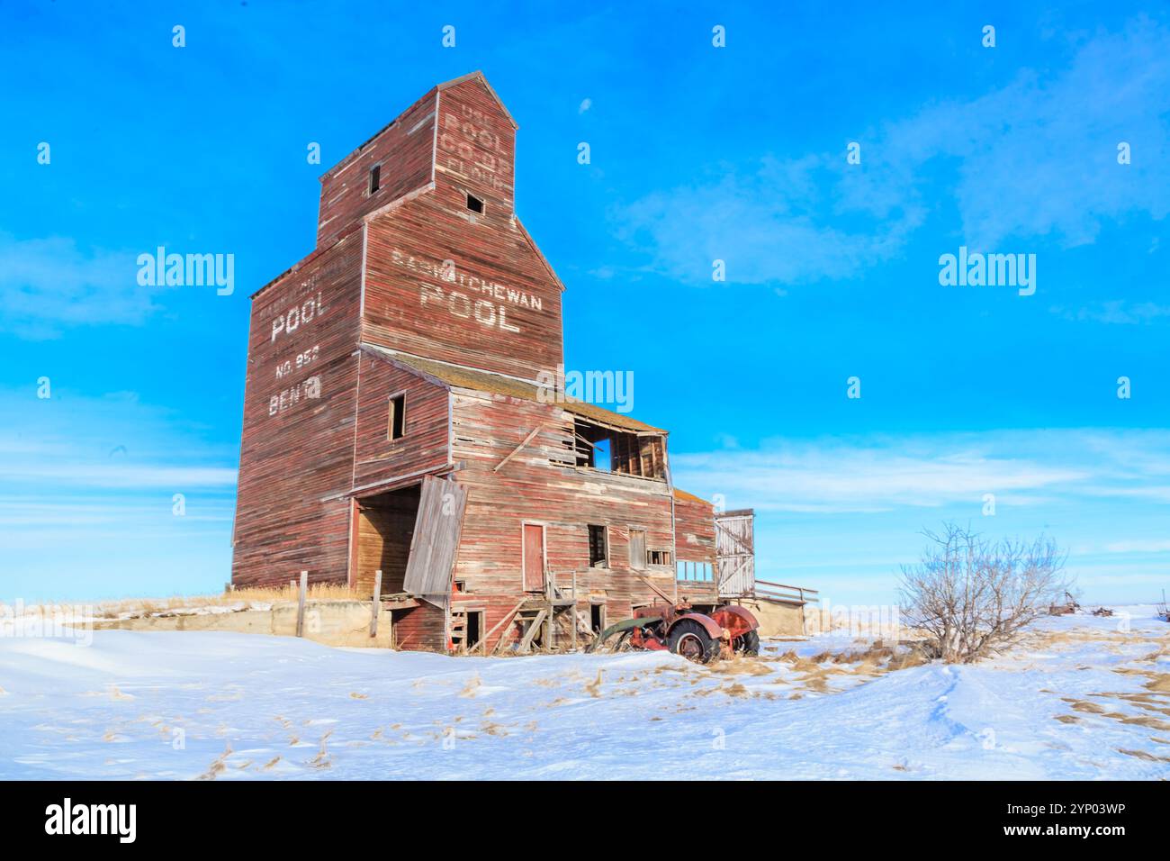 Ein altes, verlassenes Getreidesilo mit einem roten Traktor davor. Das Silo ist leer und der Traktor ist rostfrei. Der Himmel ist klar und die Sonne scheint Stockfoto