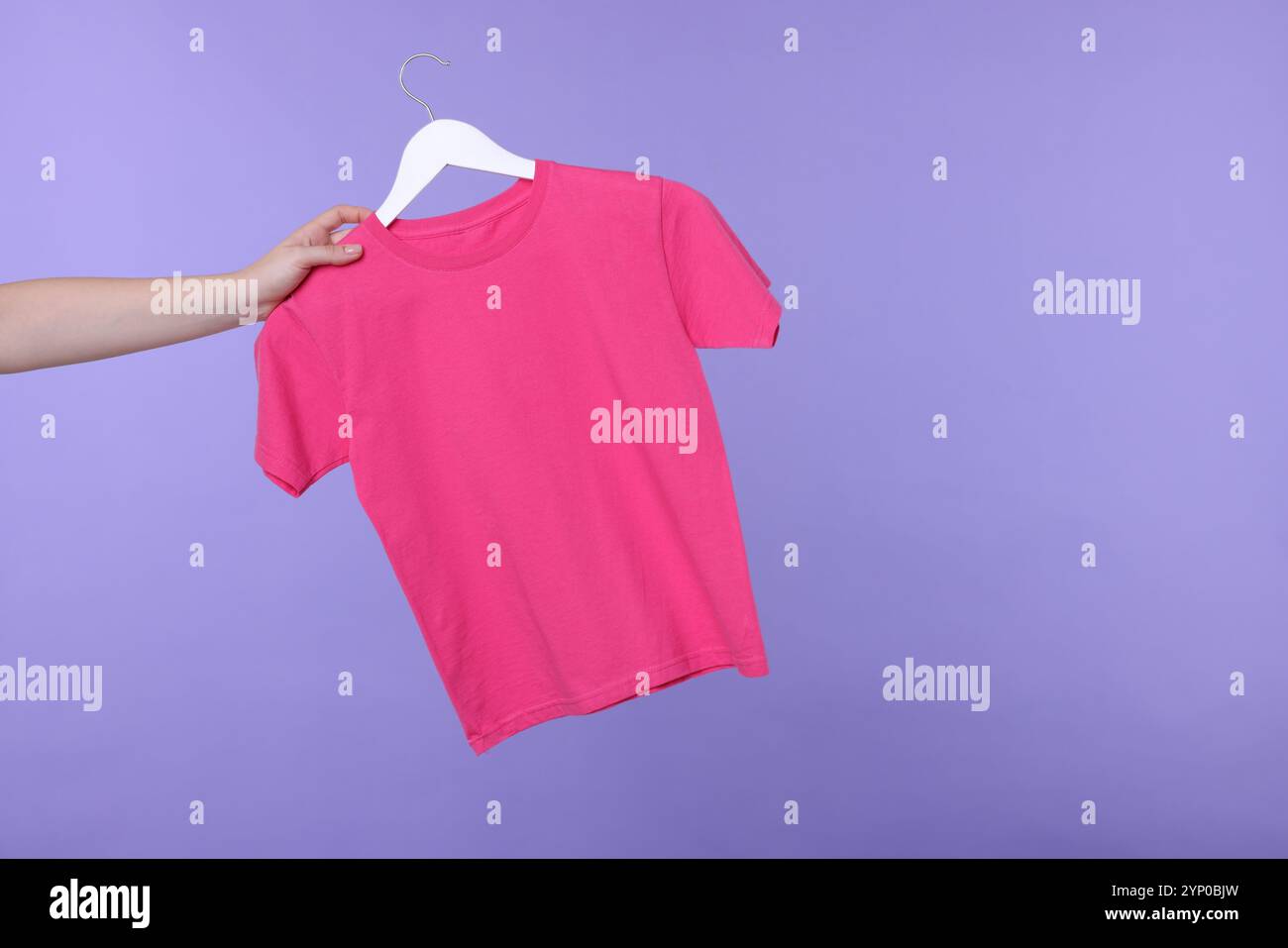 Frau, die einen Kleiderbügel mit rosa T-Shirt auf hellviolettem Hintergrund hält, Großaufnahme. Leerzeichen für Text Stockfoto